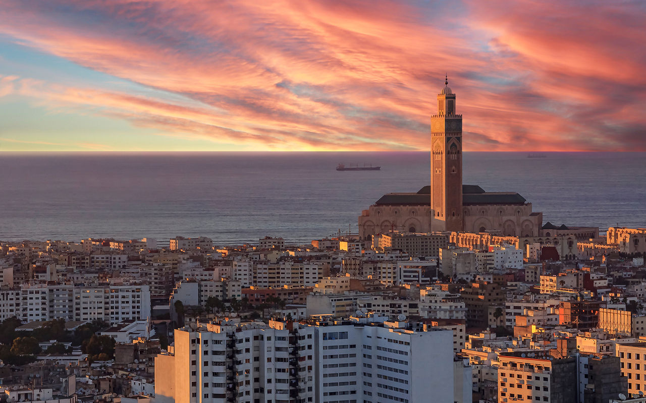 Vista aérea sobre Casablanca, con la luz del atardecer iluminando varios edificios, el cielo sobre el mar y la torre
