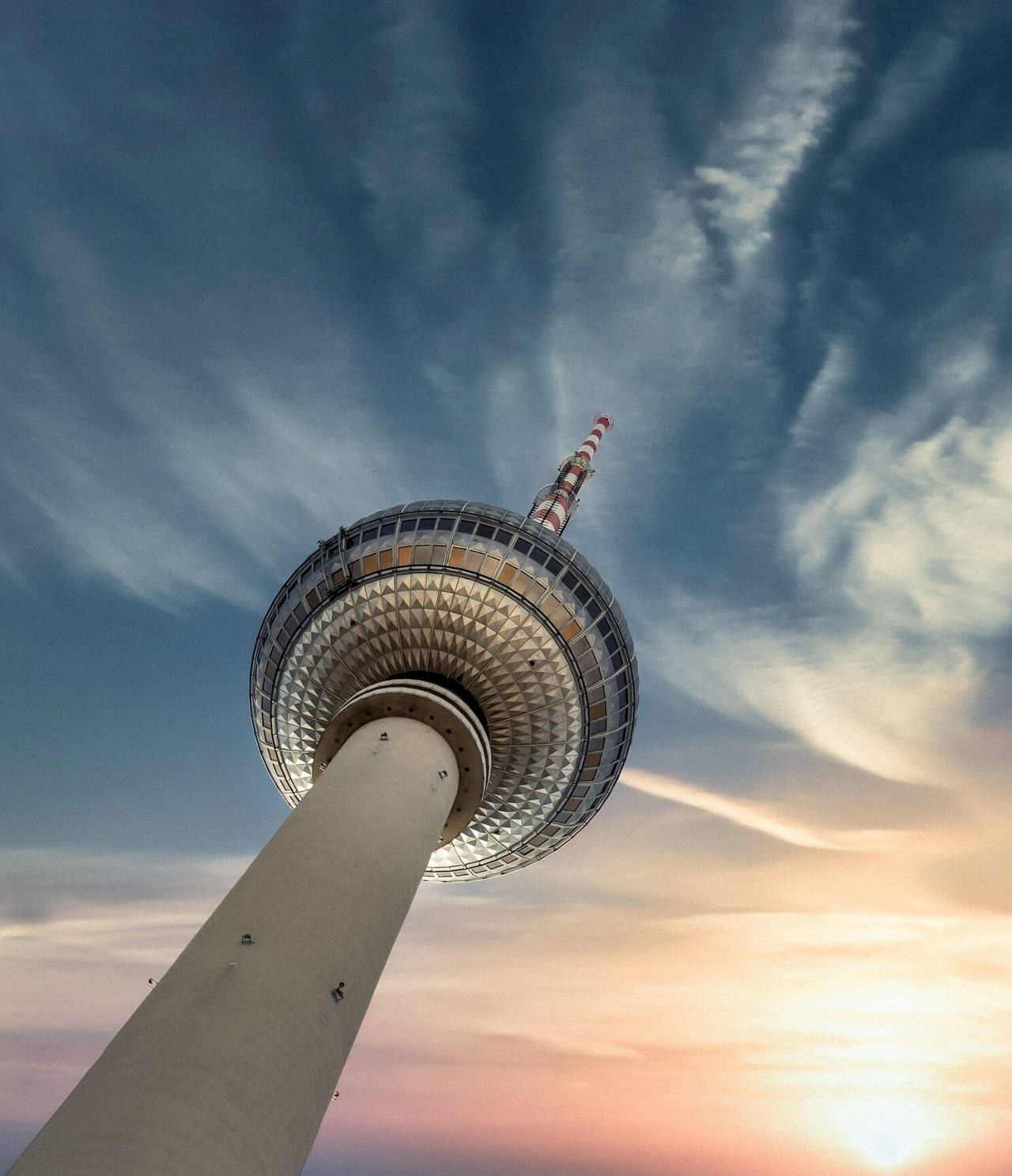 Explora Hoteles en Berlín con vistas a la torre de televisión iluminada bajo un cielo de atardecer con nubes