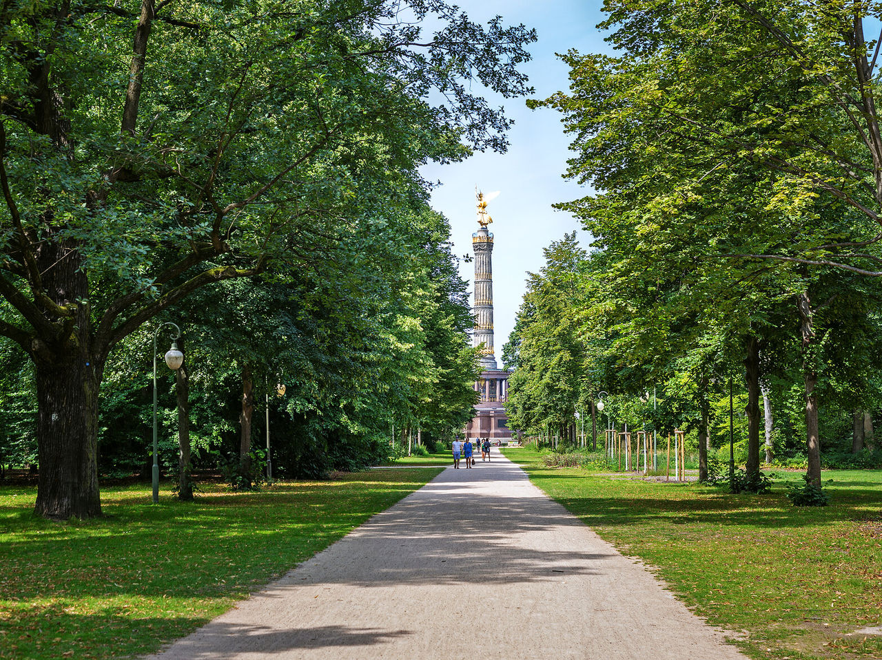 Parque con un camino rodeado de árboles, en Berlín con la famosa Columna de la Victoria al fondo