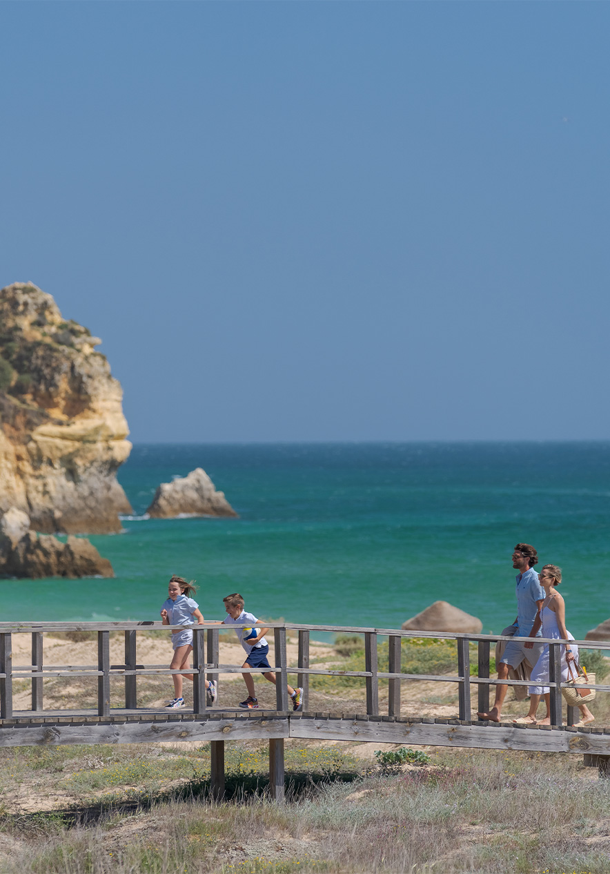 Pasadizos de madera de la playa de Alvor, con el mar de fondo y niños corriendo con sus padres