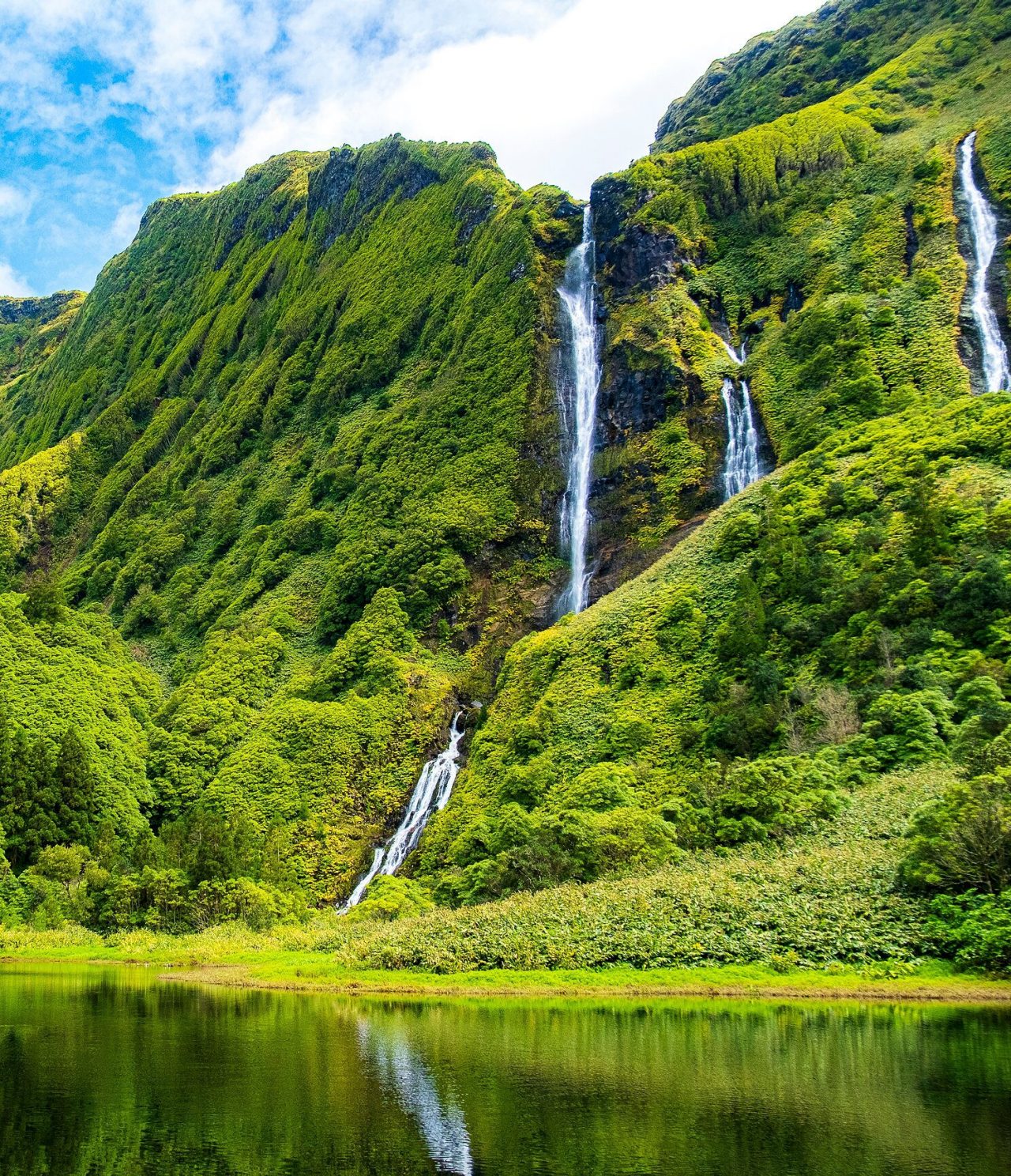 Cascada deslumbrante rodeada de montañas cubiertas de vegetación verde en la isla de Flores, Azores
