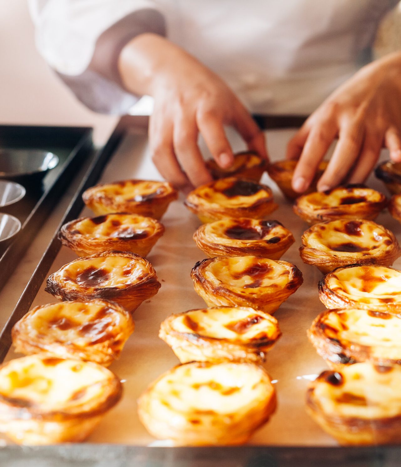 Explora Hoteles en Lisboa presentando pasteles de nata recién horneados sobre una bandeja de cocina