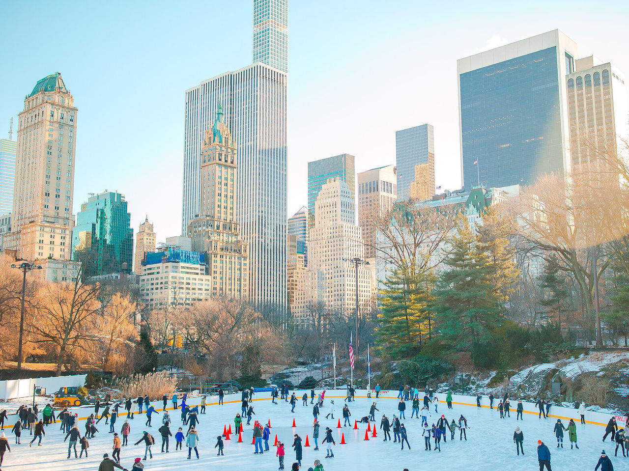 Pessoas a patinar numa pista de gelo no central park, com o horizonte da cidade no fundo