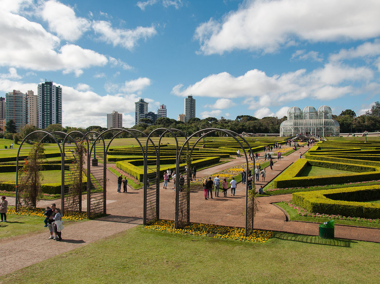 Vista lateral do Jardim Botânico de Curitiba com foco nos imponentes arcos da entrada e nos jardins floridos