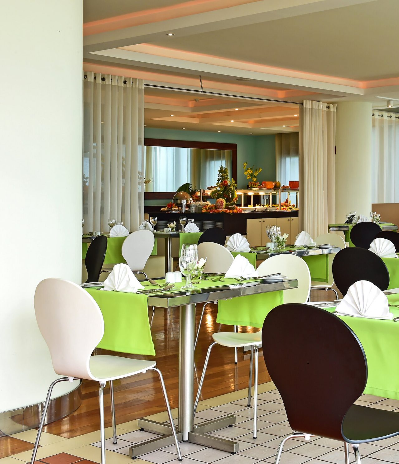 O restaurante Breezes, do Hotel 4 Estrelas Junto ao Mar no Funchal, tem várias mesas com toalha verde e um buffet ao fundo