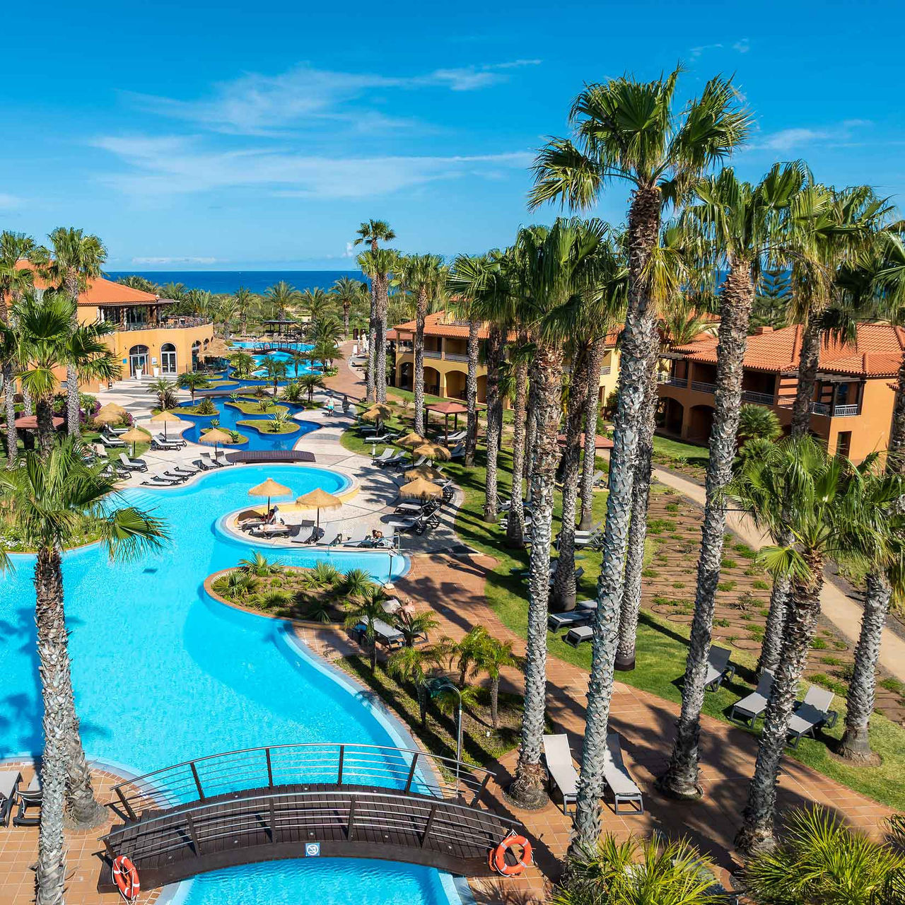 Piscina do resort de 5 estrelas no Porto Santo, rodeada de palmeiras tropicais, espreguiçadeiras e jardim. 