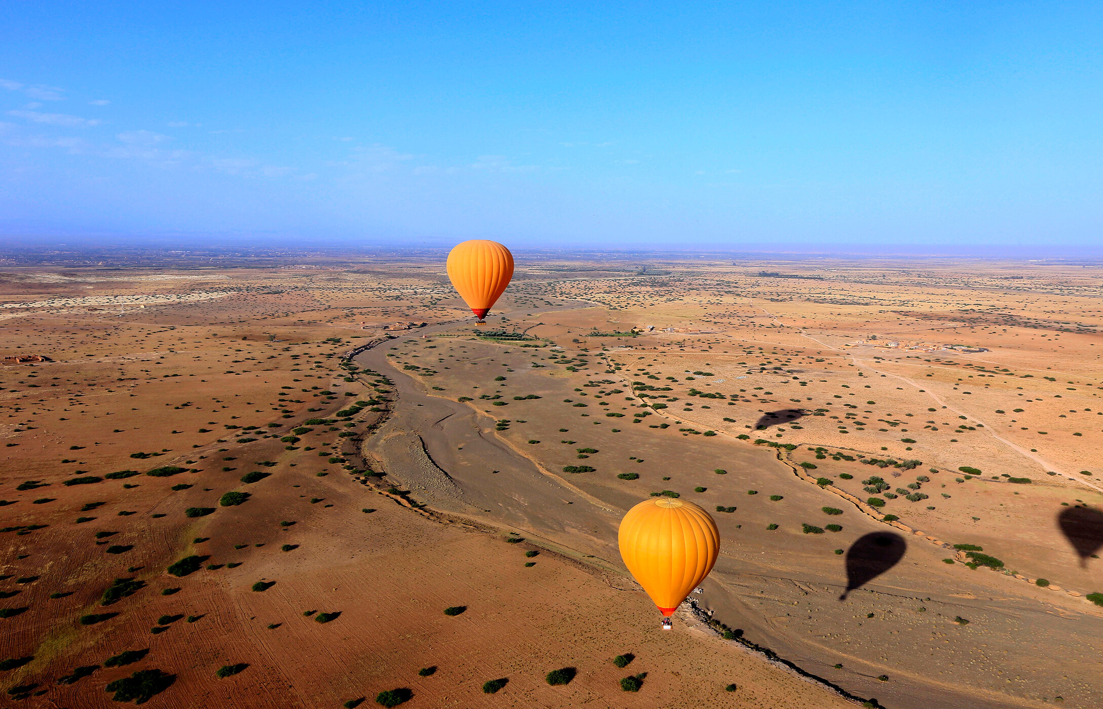 Luftaufnahme einer Ebene in der Nähe von Marrakesch, mit zwei orangefarbenen Heißluftballons, die über die Ebene fliegen