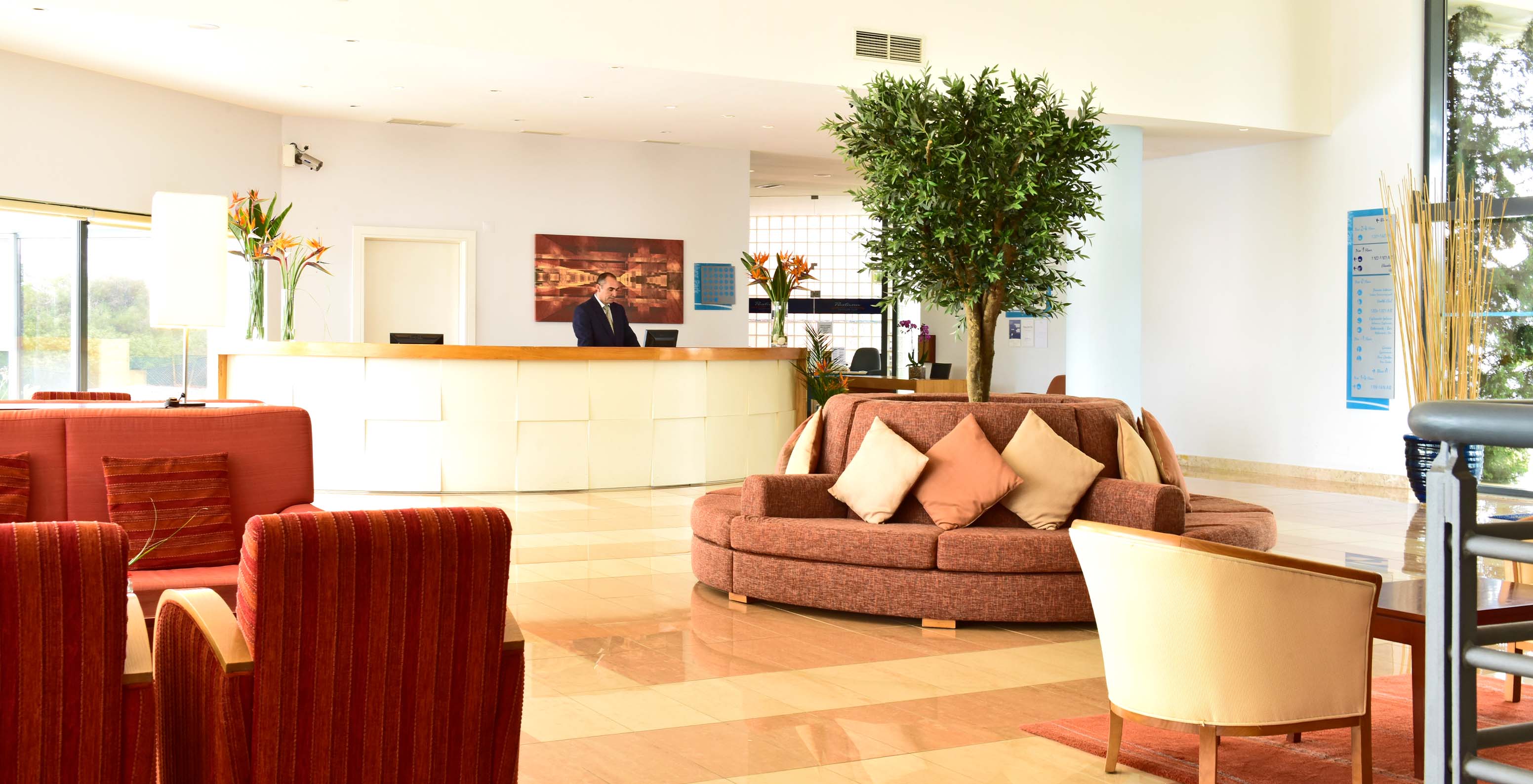 Rezeption des Hotels Pestana Alvor Park mit roten Sofas und Sesseln, Blumen in Vasen und einem Baum in der Mitte