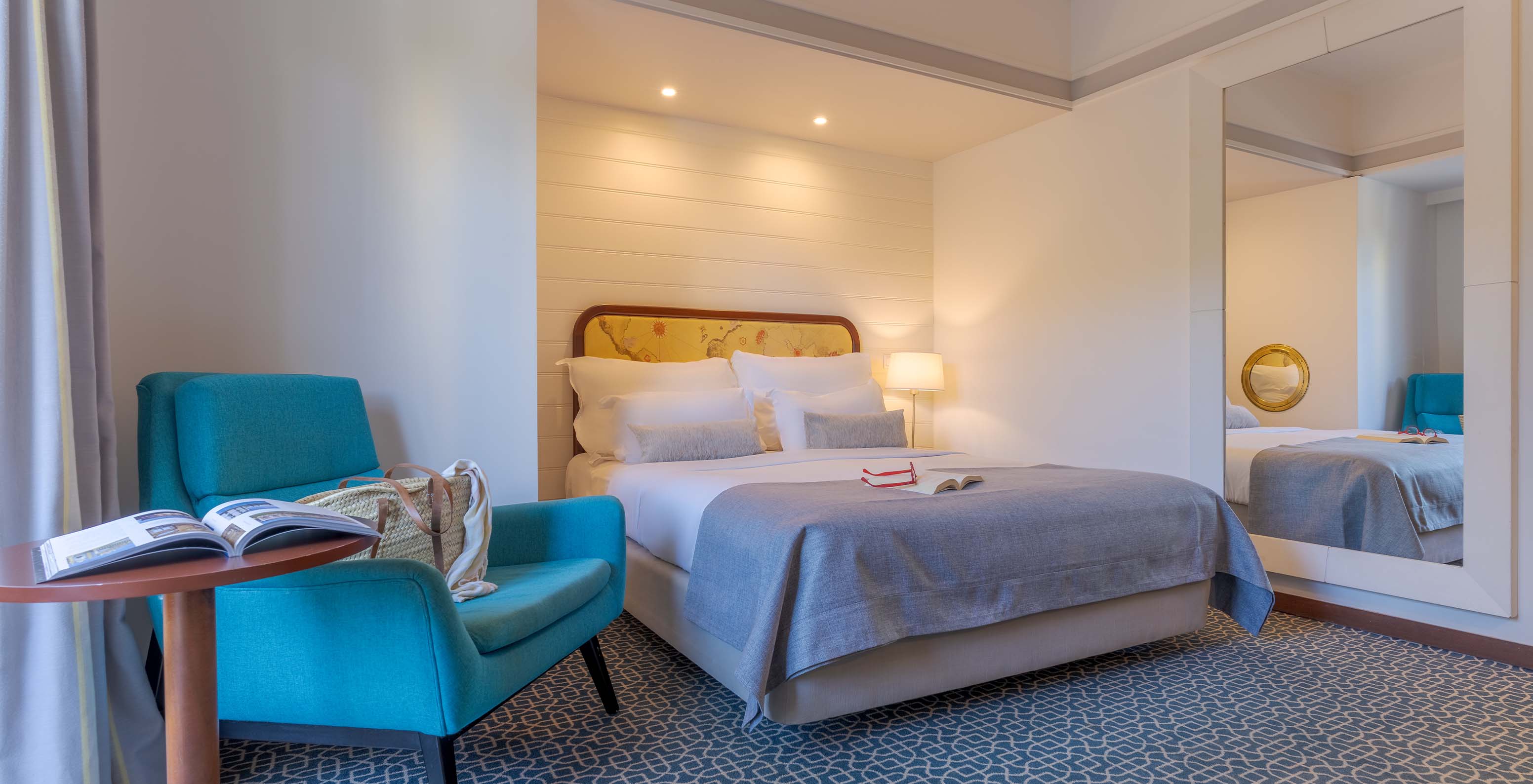 Das Deluxe im Pestana Alvor Praia hat ein Doppelbett, einen Tisch mit einem blauen Sessel und einen Spiegel