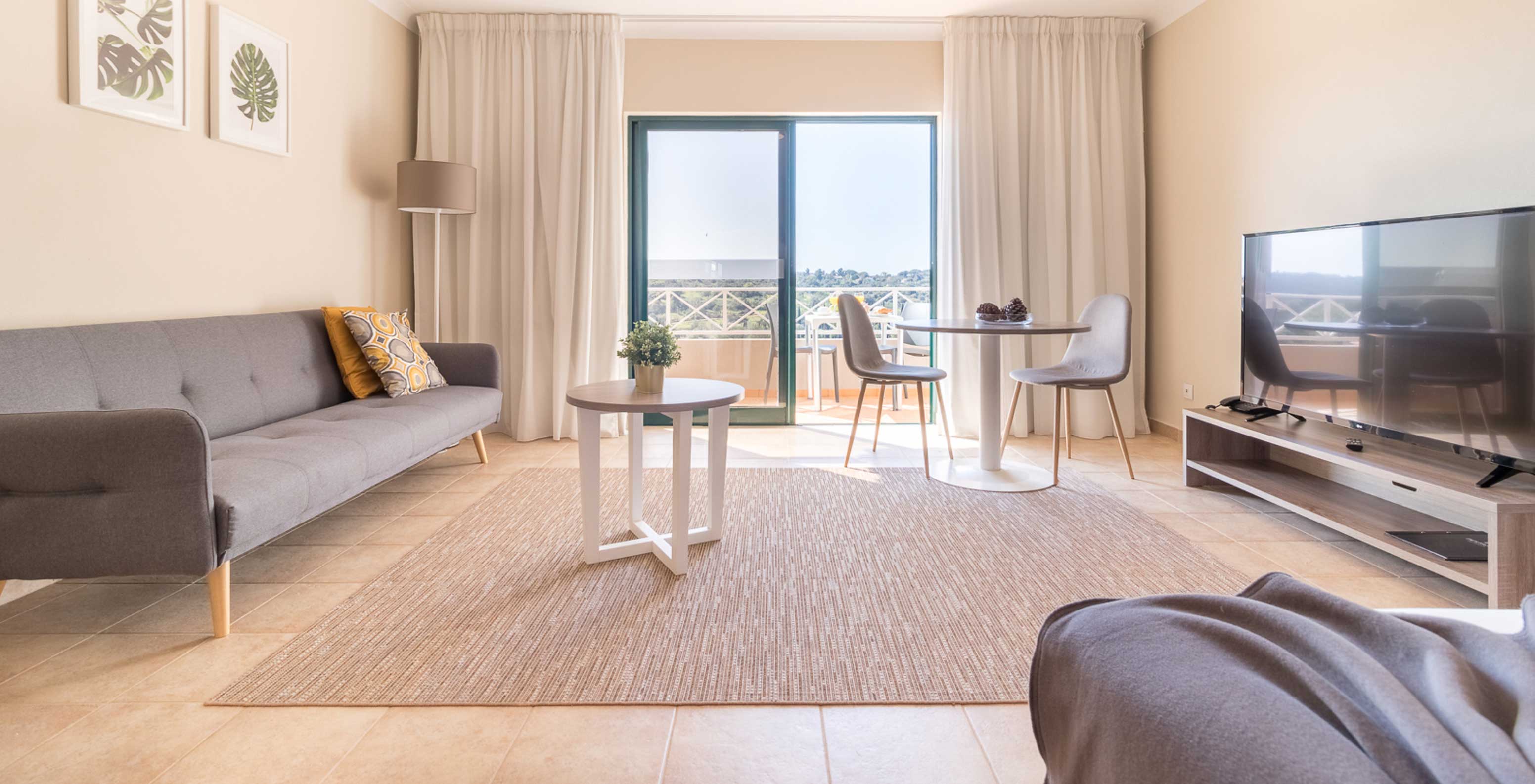 Das Studio im Pestana Gramacho Residences hat ein Wohnzimmer mit grauem Sofa, TV, Tisch und hellem Balkon