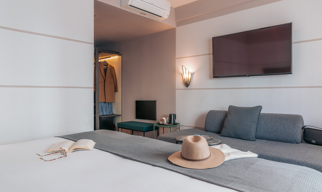 Das Double Classic im Pestana Lisboa Vintage hat Doppelbett mit grauer Decke, graues Sofa und Fernseher