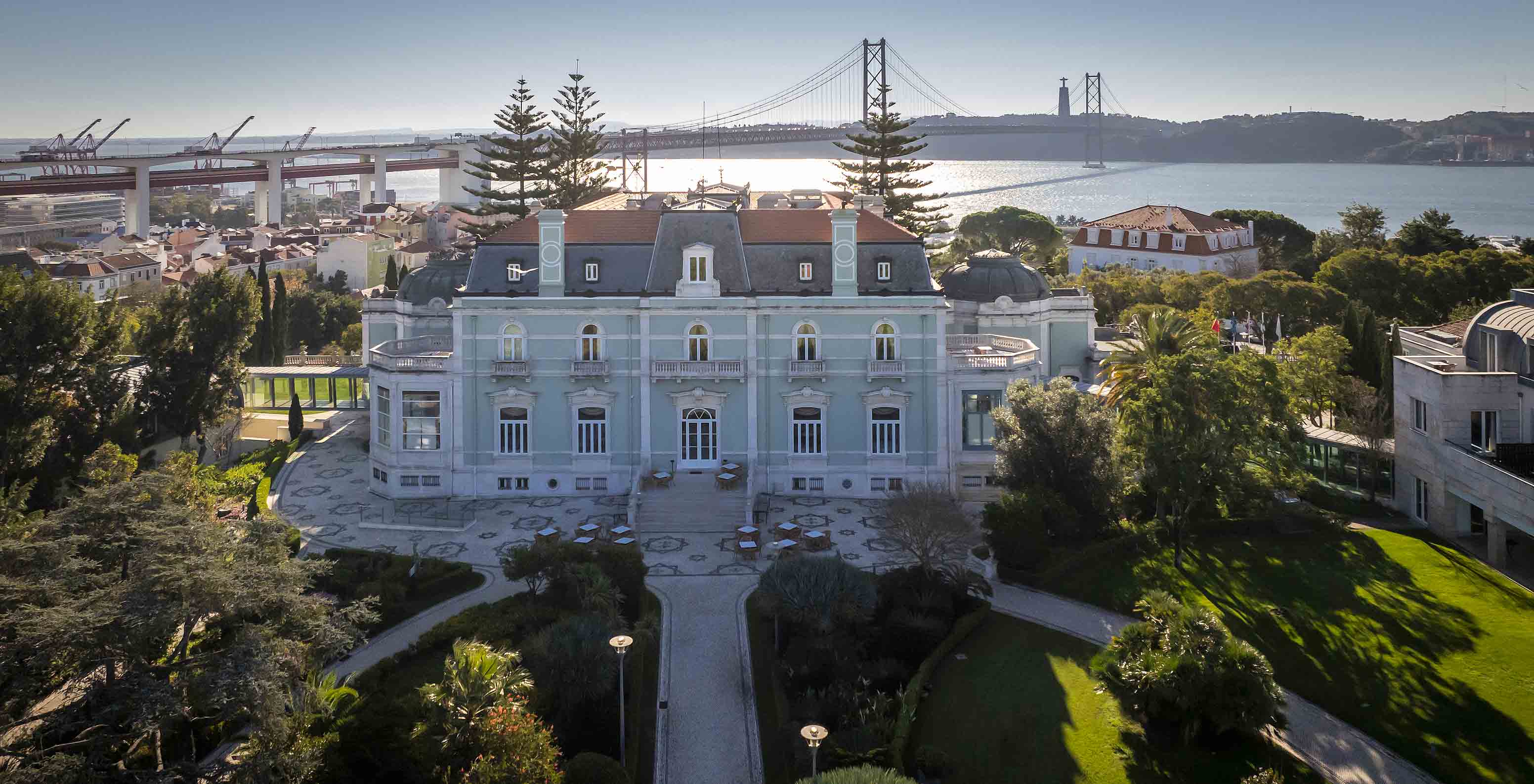 Luftaufnahme des Hauptgebäudes des Pestana Palace mit der Brücke des 25. April, dem Fluss Tejo und Cristo Rei im Hintergrund