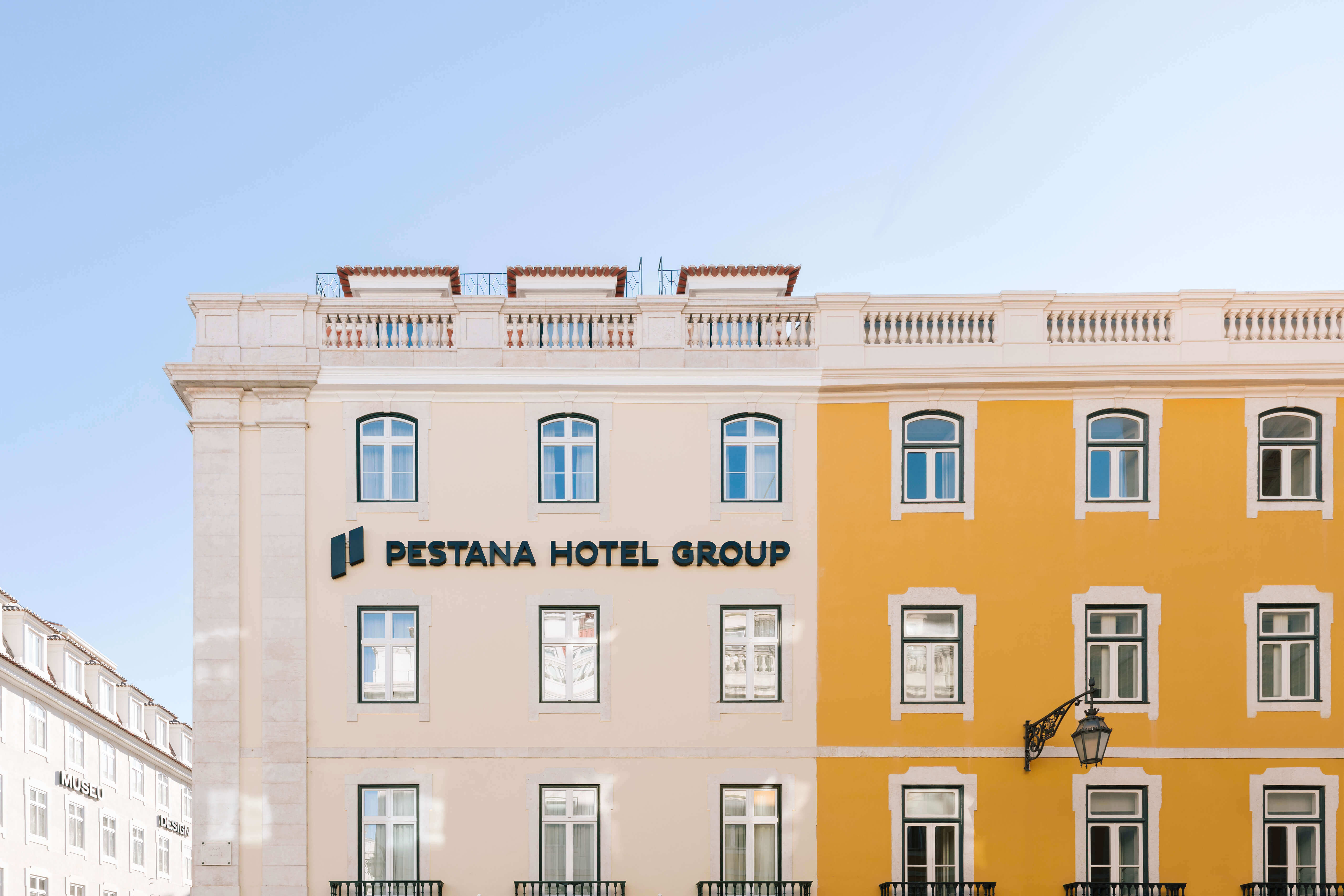 Seitenansicht des weißen und orangefarbenen Gebäudes des Pestana Rua Augusta Lisboa mit Pestana Hotel Group Logo