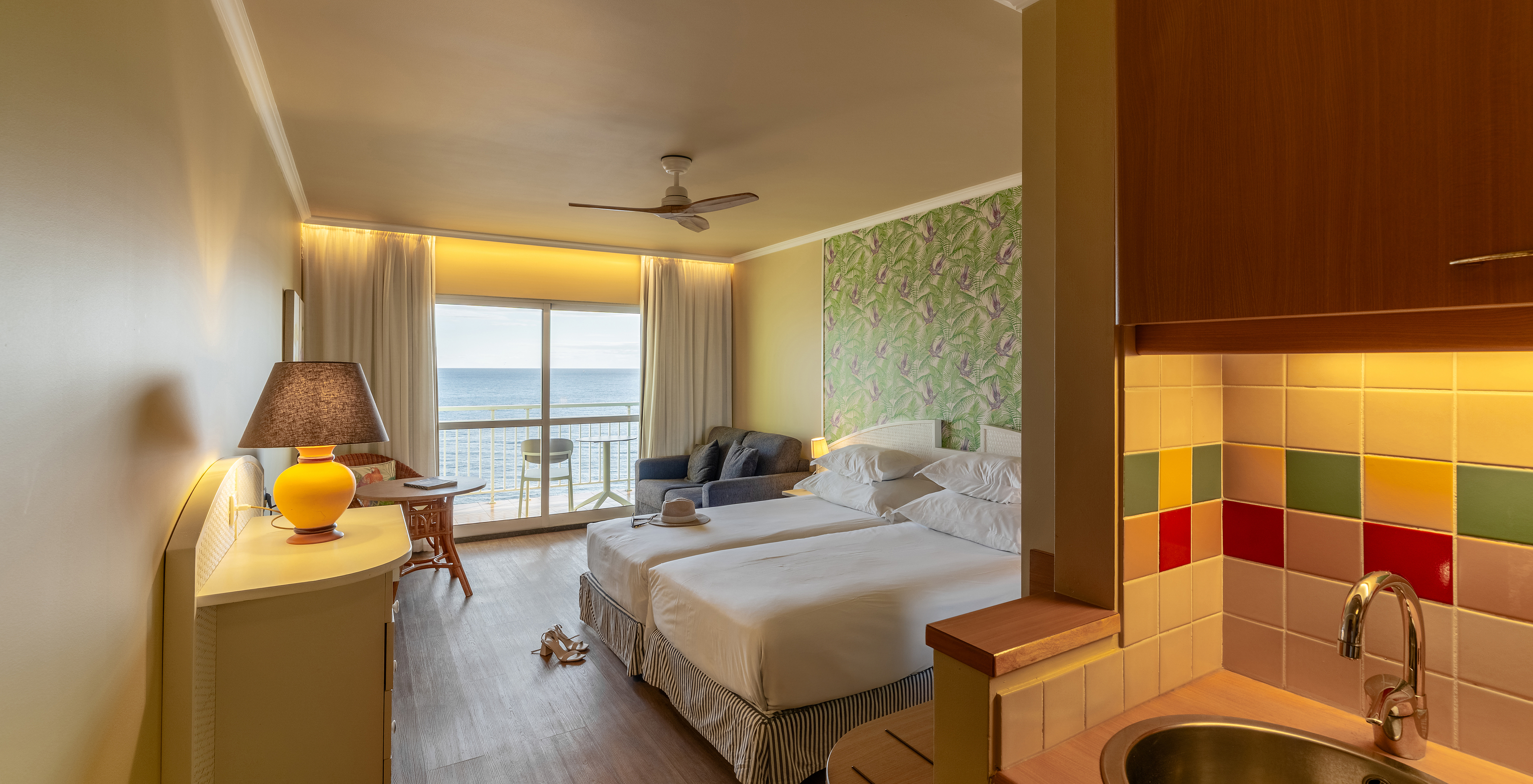 Das Premium Sea View im Pestana Ocean Bay All Inclusive verfügt über ein Doppelbett, Palmen-Tapete, ein Sofa und einen Balkon