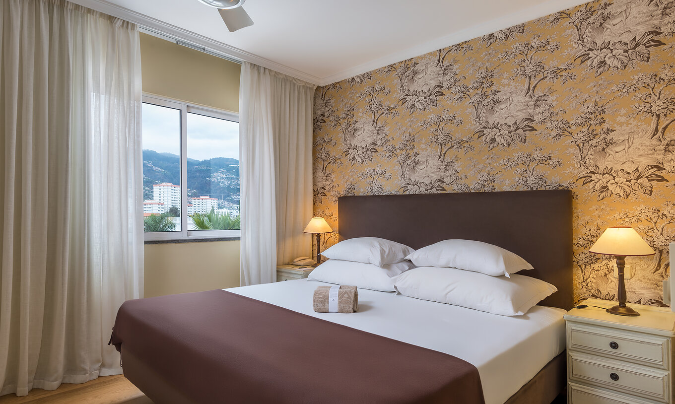 Superior Familie Pestana Village hat ein Doppelbett mit Kopfteil und braunem Überwurf, Blumentapete und Balkon