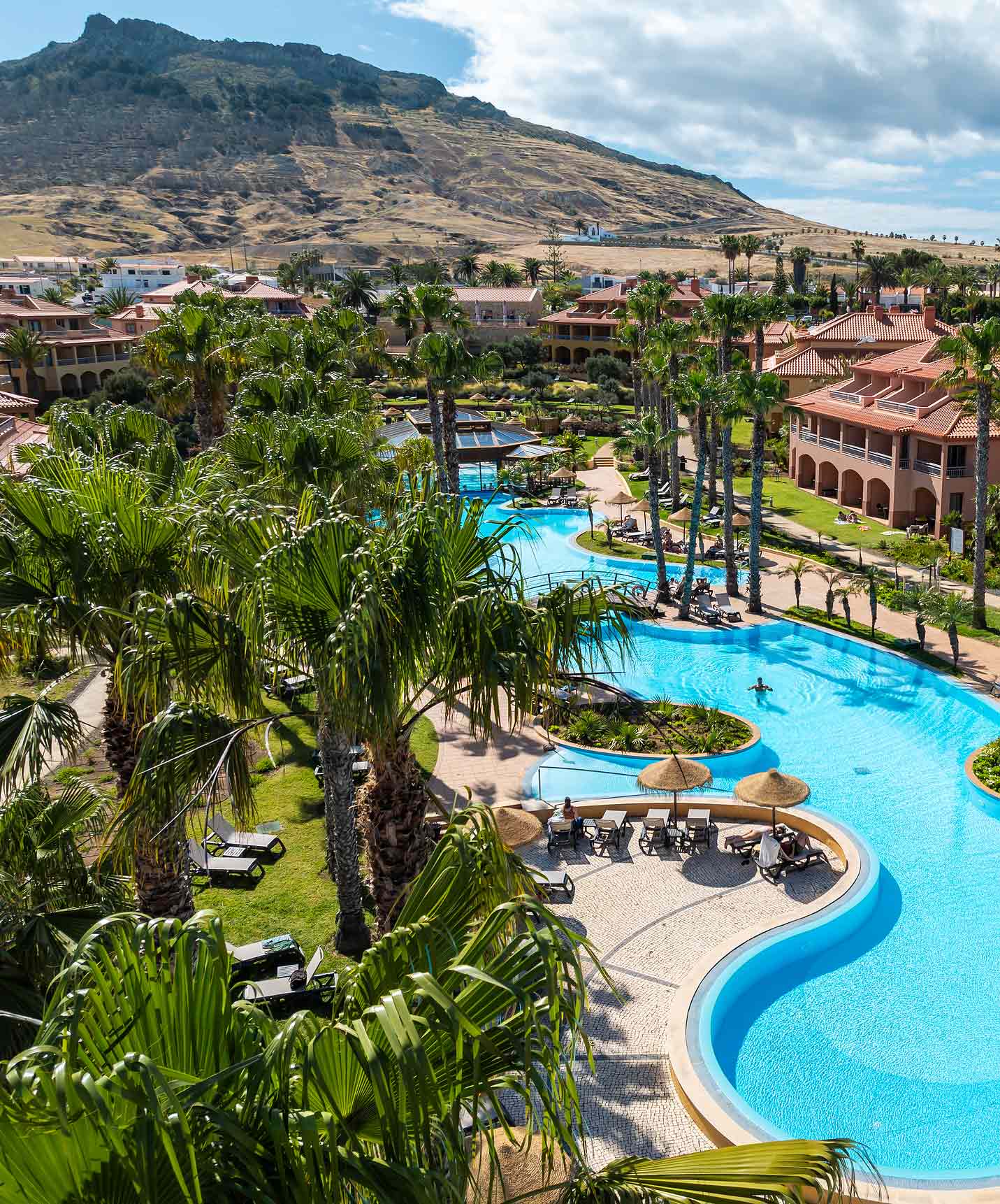 Blick auf den Außenpool des Pestana Porto Santo All Inclusive, umgeben von Garten, Palmen und Sonnenliegen.