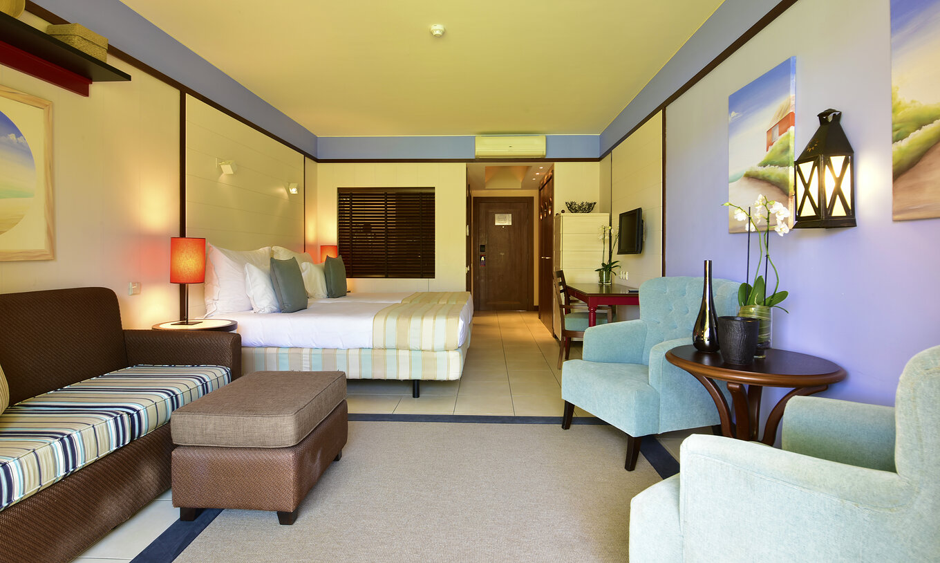 Das Doppelzimmer Poolblick hat ein Sofa, zwei Sessel, zwei Betten, Fernseher und Schreibtisch 