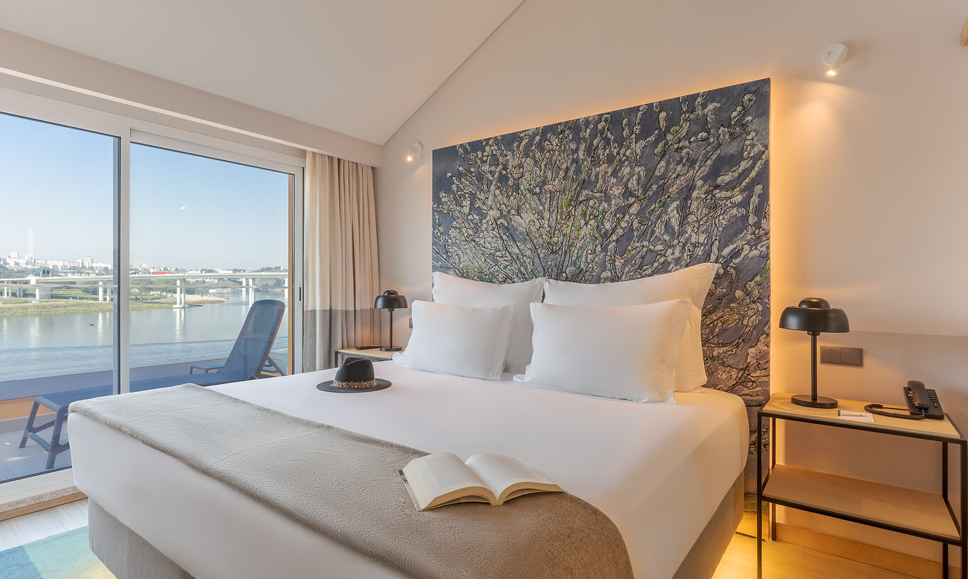 Die Suite Douro im Pestana Douro Riverside hat ein Doppelbett mit Nachttisch und Balkon mit Blick auf den Fluss