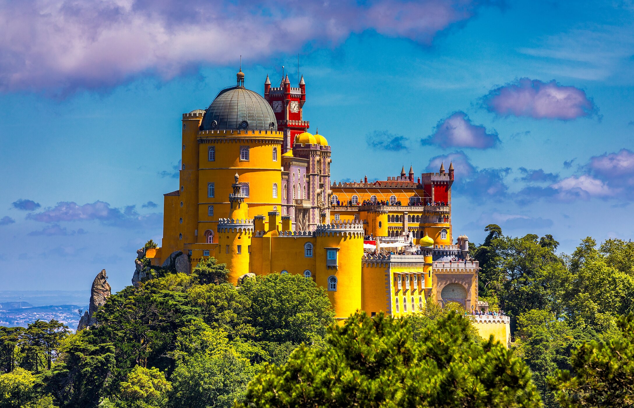 Luftaufnahme des Palácio da Pena in Sintra, mit seinen lebhaften Farben, umgeben von Vegetation unter blauem Himmel.