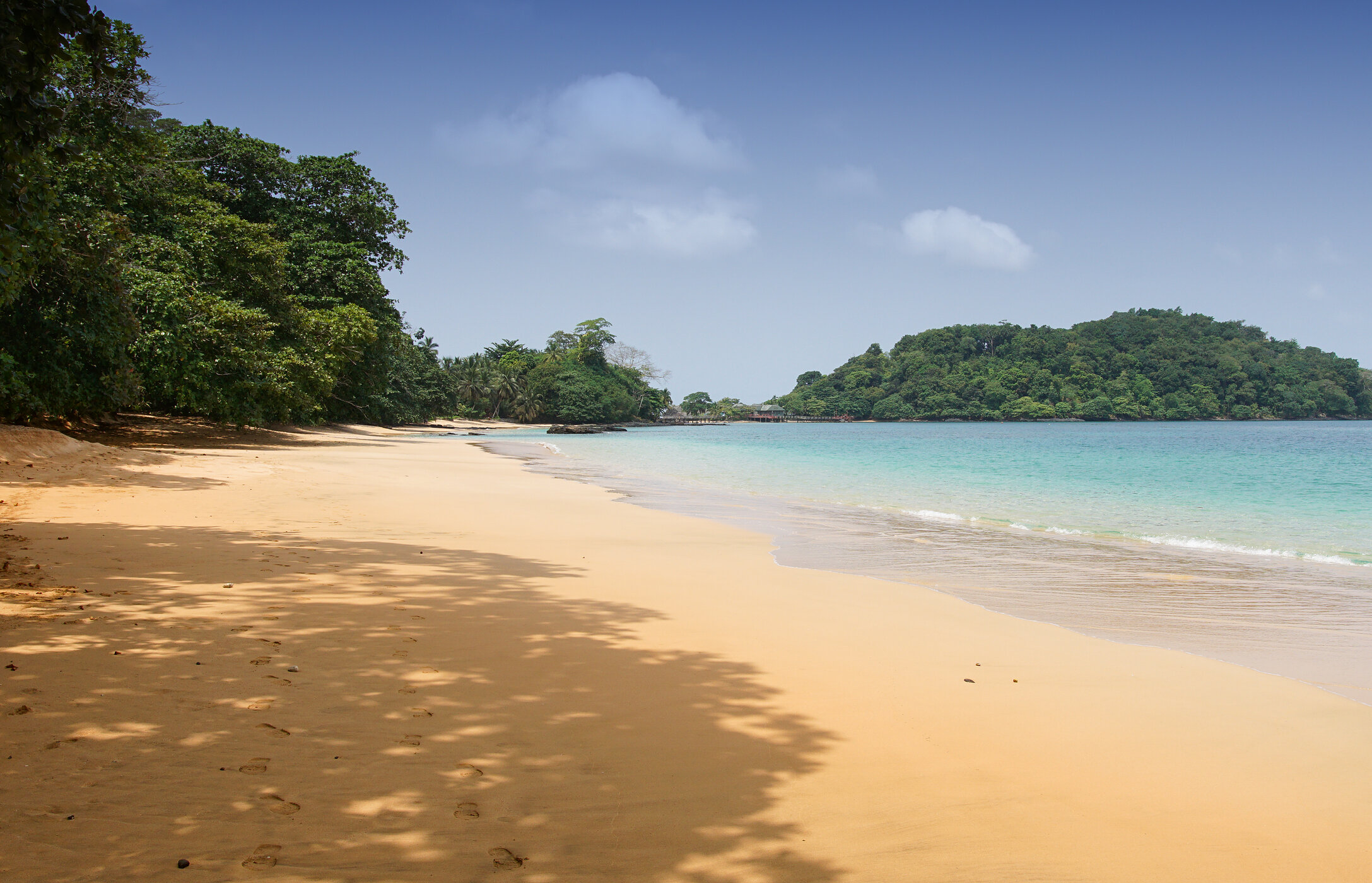 Blick auf den Coco-Strand in São Tomé und Príncipe, mit goldenem Sand, ruhigem kristallklarem Wasser und Vegetation.