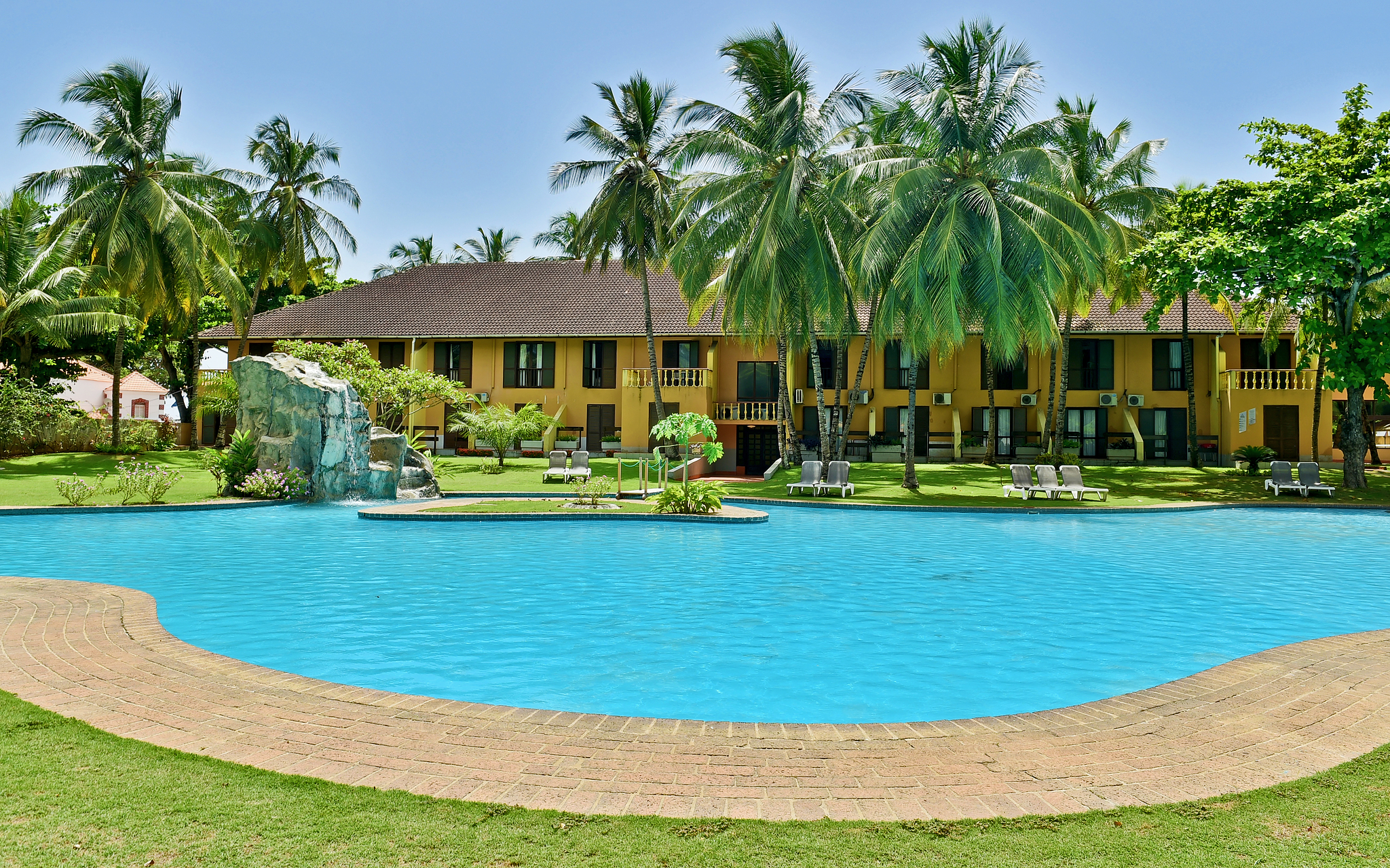 Gelbes Gebäude mit vielen Fenstern, Außenpool, Palmen und Liegen eines 4-Sterne-Hotels in São Tomé