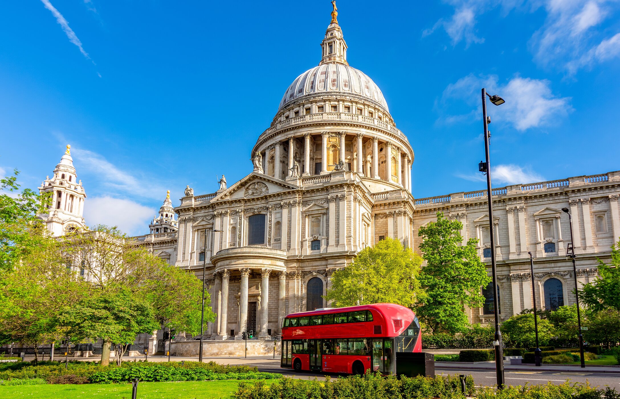 Stadtansicht der St Paul's Kathedrale in London, mit einem roten Bus vorne und einem Garten