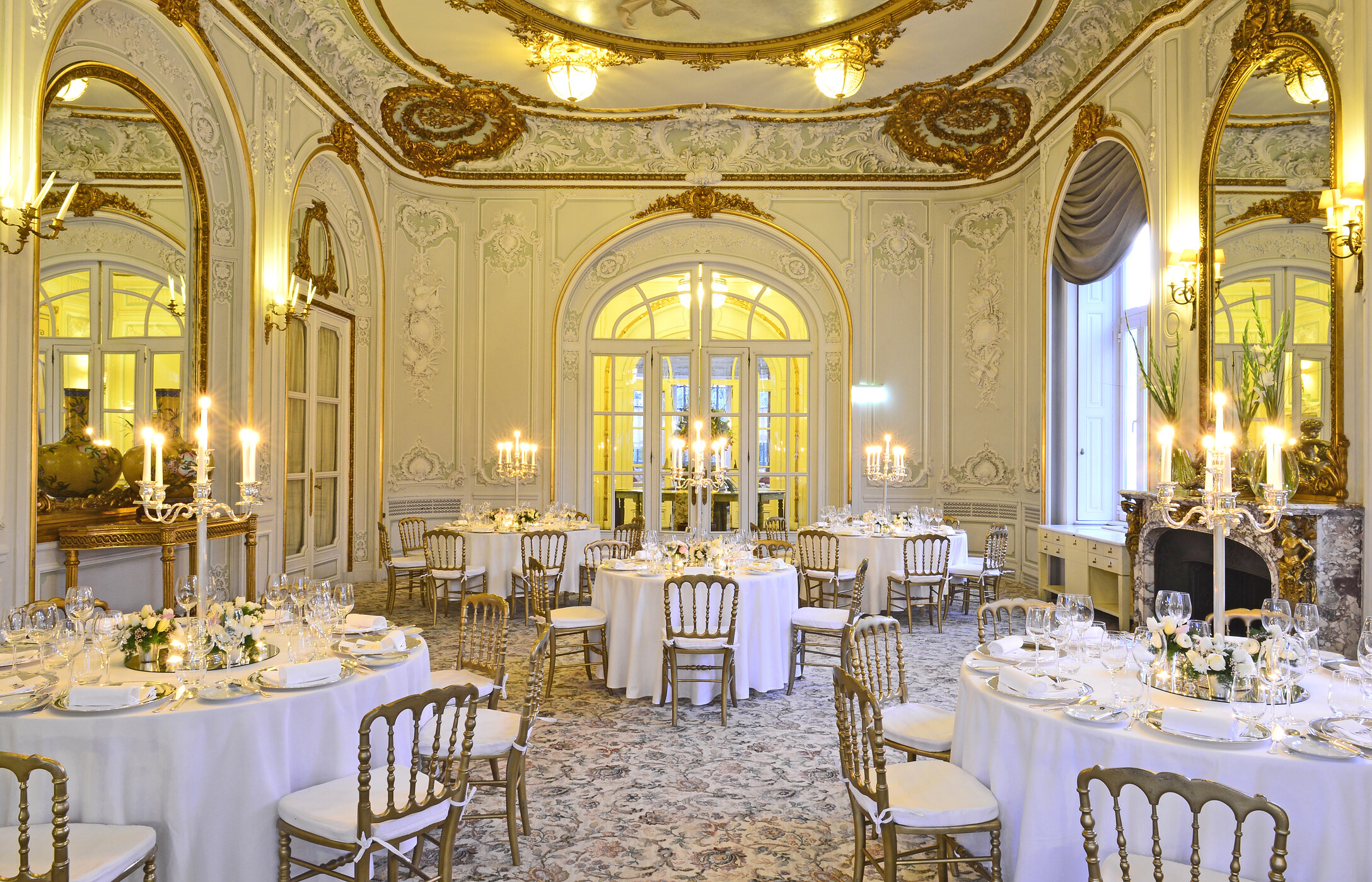 Hochzeit in einem eleganten Raum, mit gemustertem Teppich, Wänden mit Goldakzenten und Tischen mit Blumengestecken