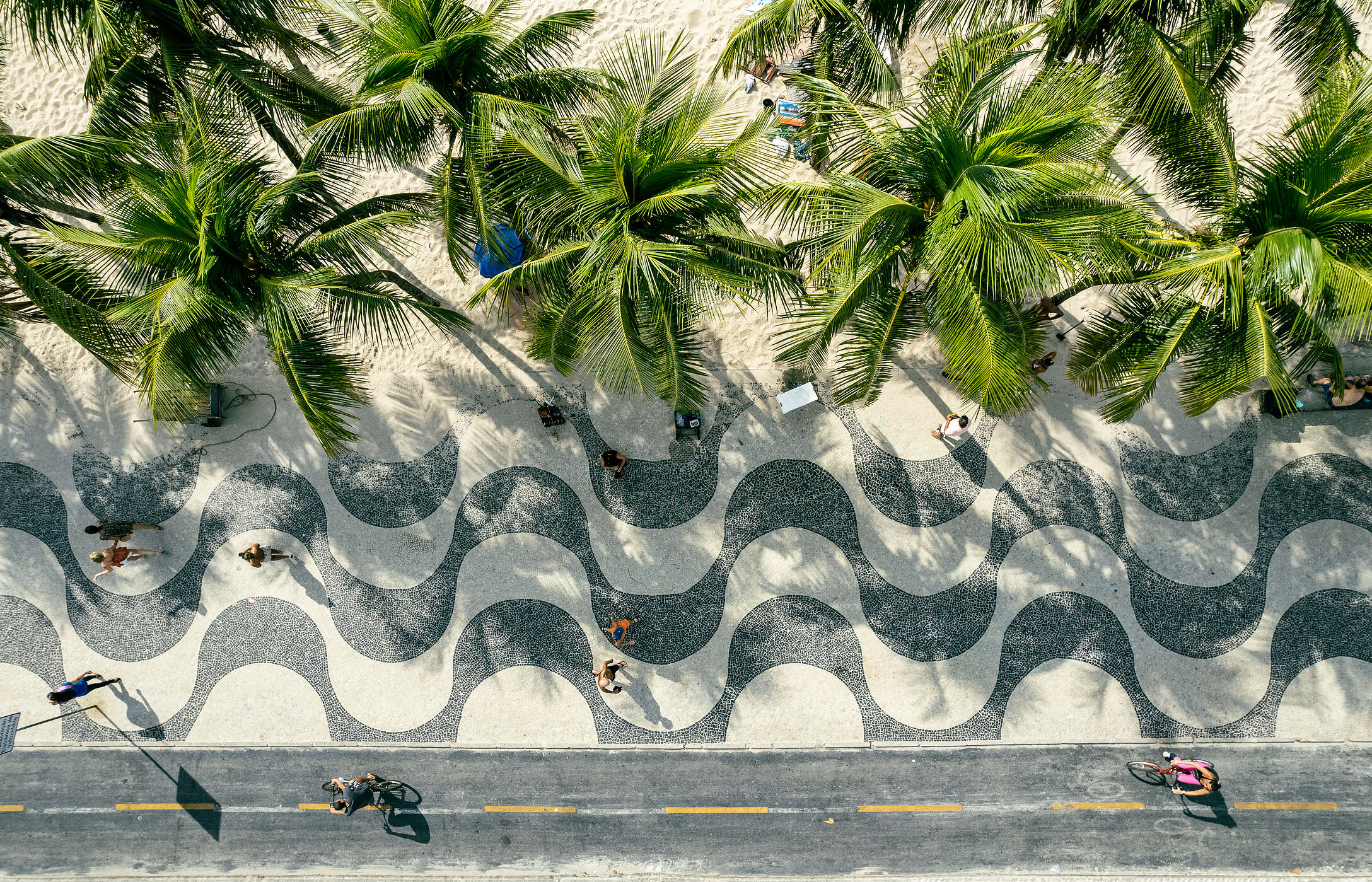 Aerial view of Avenida Atlântica's sidewalk with palm trees and white sand in front of Copacabana Beach in Brazil