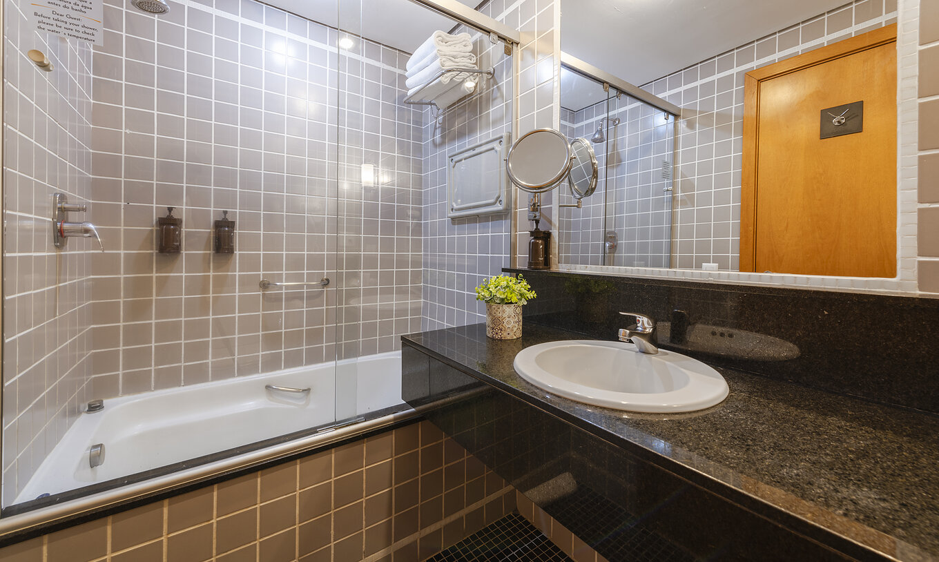 The Twin Standard at Pestana Curitiba has a bathroom with a bathtub in gray tiles and a countertop with a sink