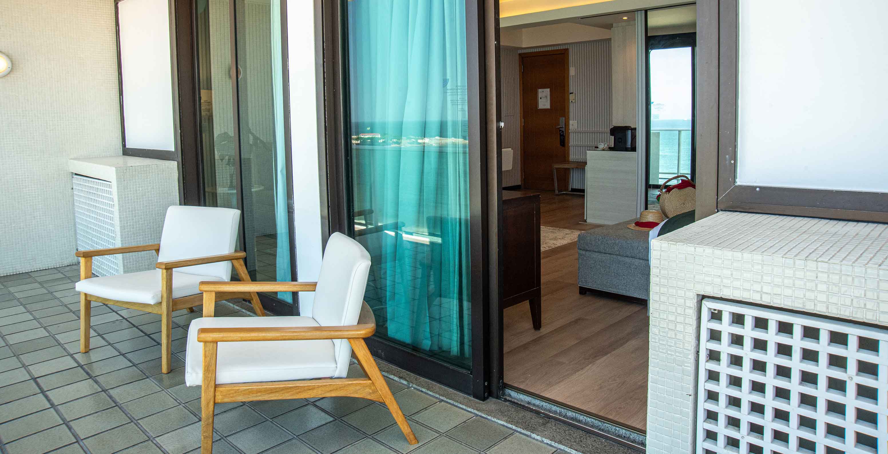 The Oceanic Suite at Pestana Rio Atlântica has a balcony with wooden chairs and room access.