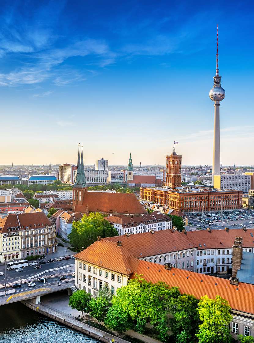 Aerial view over the city of Berlin, with a bridge with cars passing, several buildings, and the iconic television tower