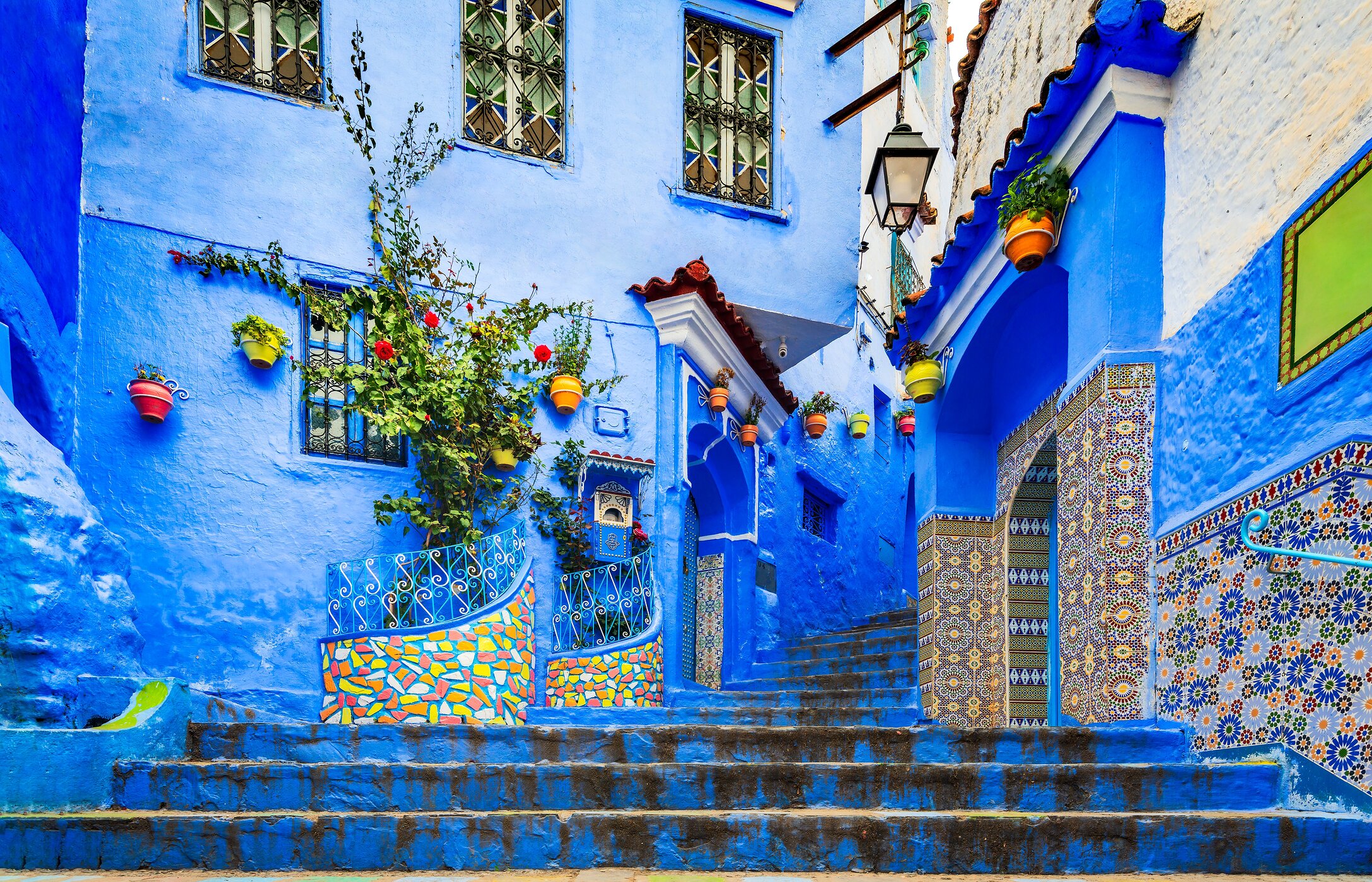 Staircase in Chefchaouen, with blue buildings, patterned tiles, and hanging pots.