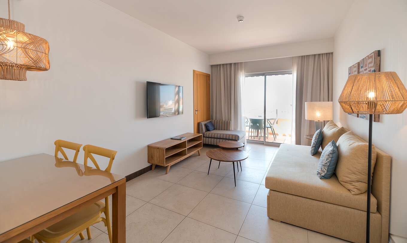 Apartment T1 Sea View at Pestana Alvor Beach Villas has a living room with sofa, TV and window with balcony access