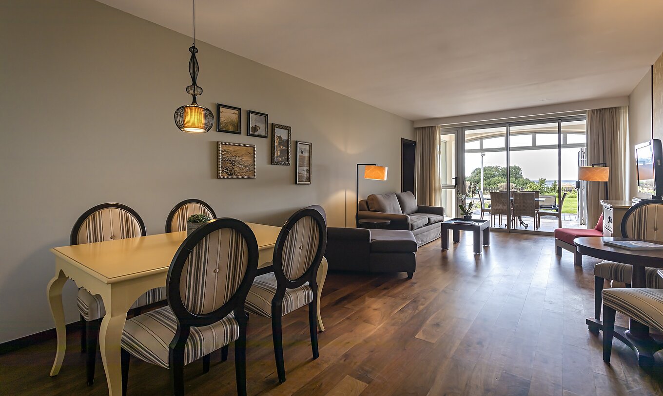 The Cliff Suite T2 at Pestana Alvor Praia has a living room with two sofas, a television, a dining table, and a porch