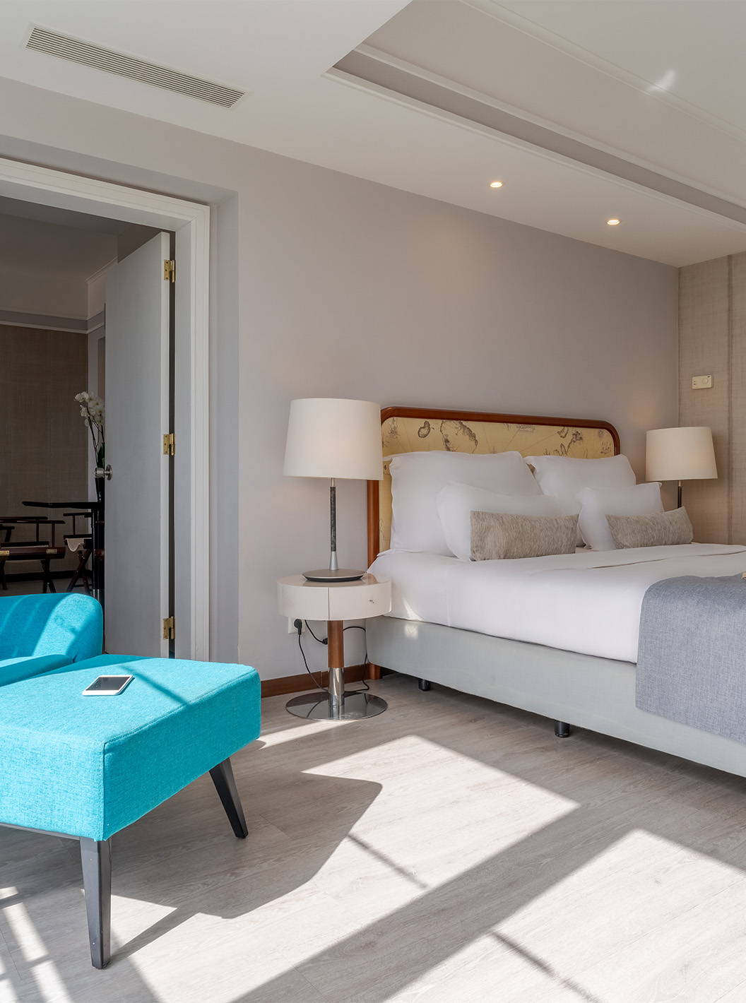 The Sea View Suite at Pestana Alvor Praia has a double bed with a blue armchair, lamps, and wooden flooring