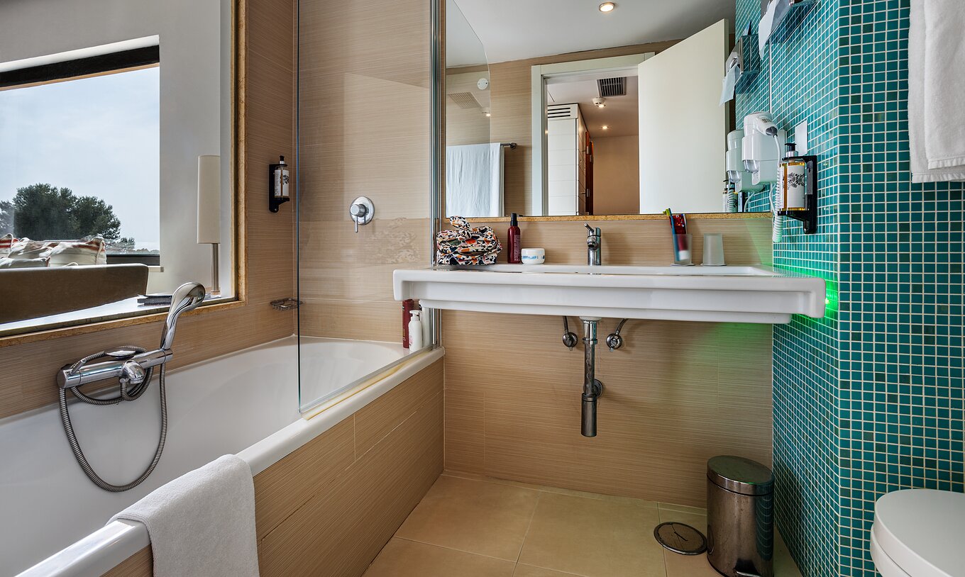 The Deluxe Garden View room at Pestana Dom João II features a bathroom with a sink, mirror, and bathtub
