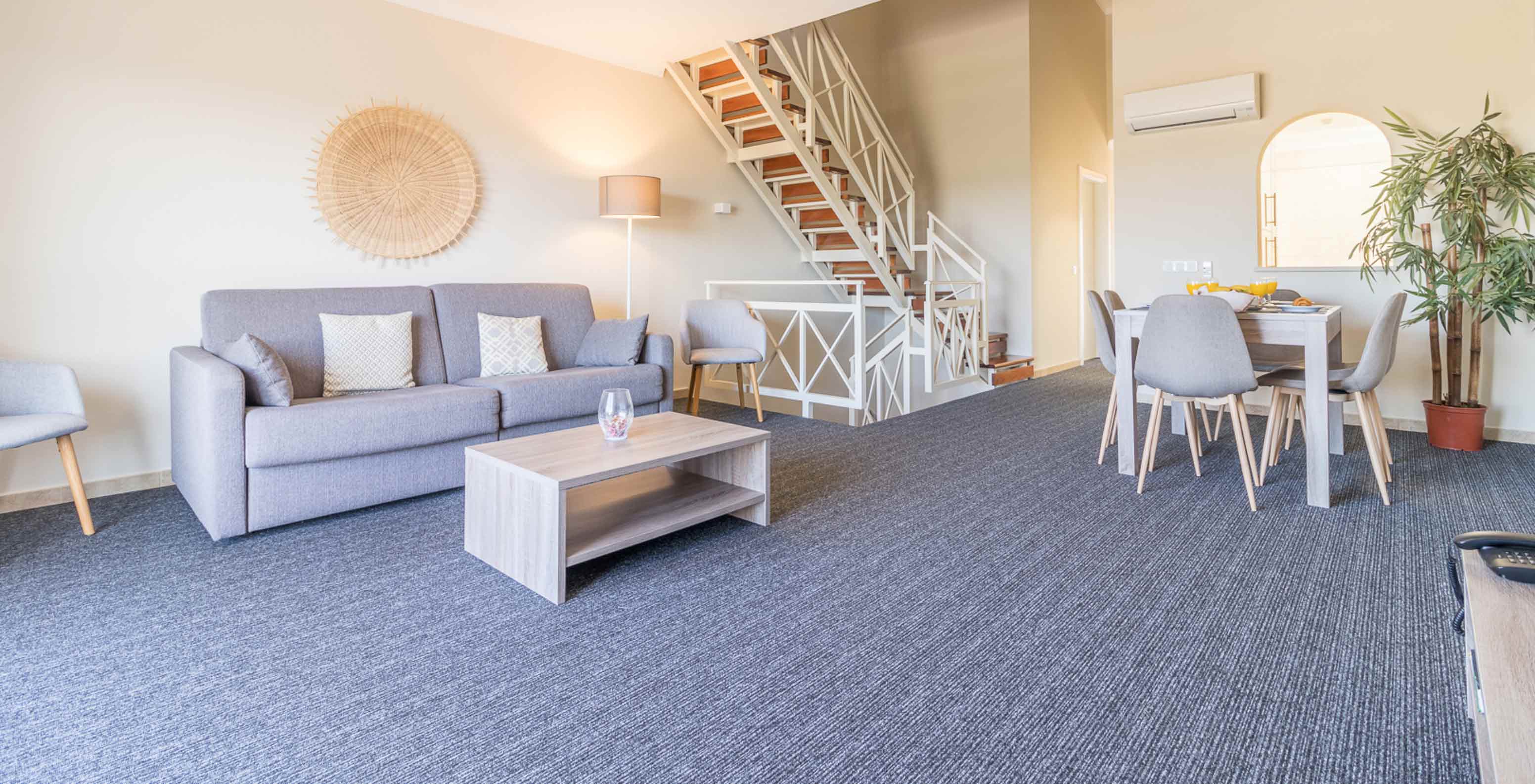 The two-bedroom apartment at Pestana Gramacho has a living room with grey sofa, coffee table and stairs in the back