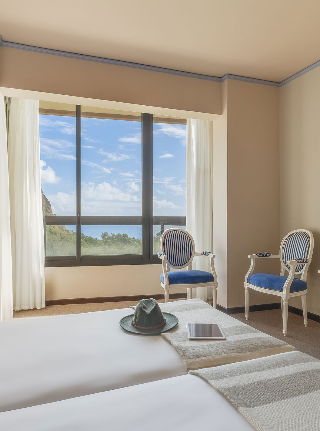 Standard Garden View room at Pestana Bahia Praia has two chairs near the window with a view of the green island landscape