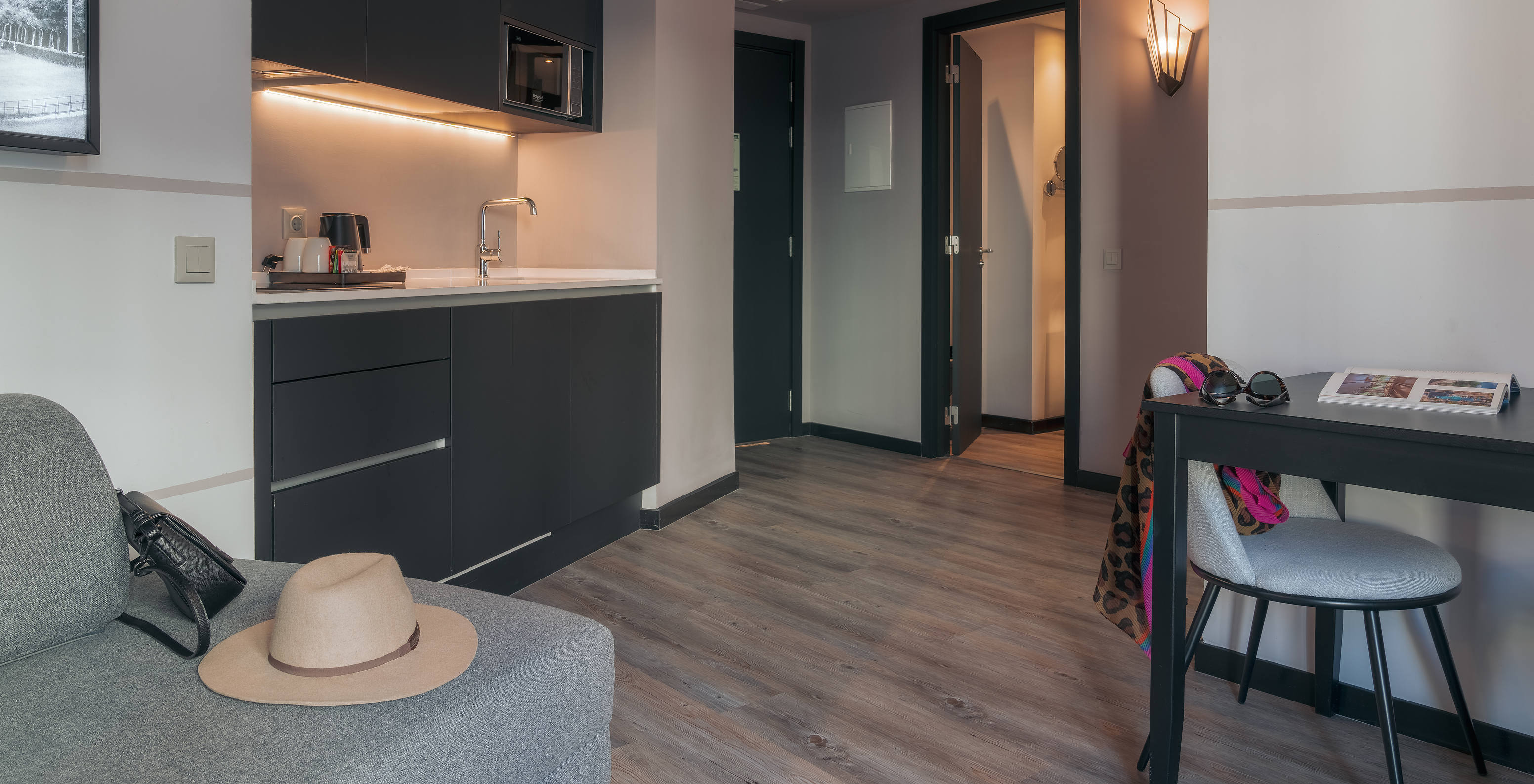 The Double Deluxe Studio at Pestana Lisboa Vintage has a kitchenette with microwave, a table with chair and a gray sofa