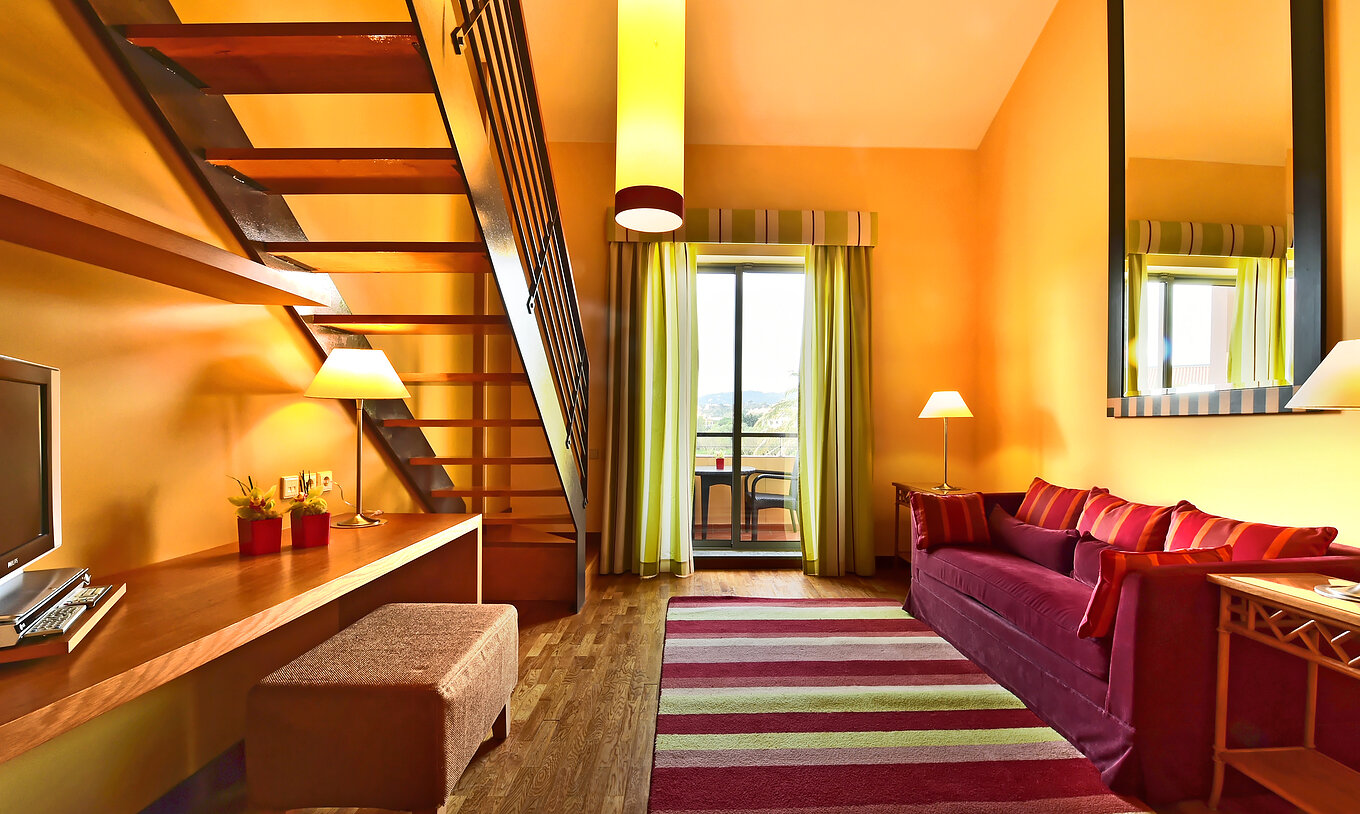 The Family Mezzanine Suite of Pestana Sintra Golf has a room with a large sofa, mirror, and a window with balcony access