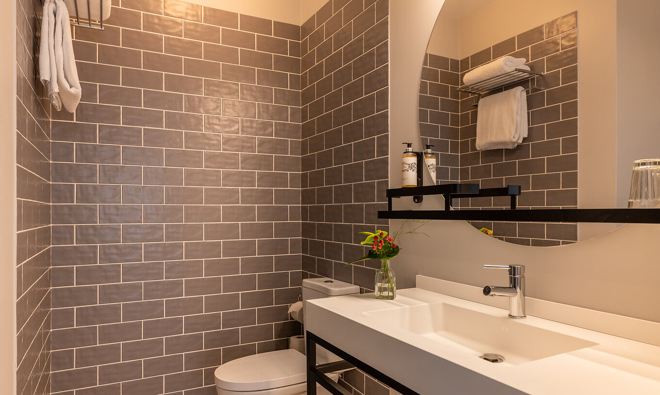 The Cozy room at Pestana Fisherman Village features a bathroom with gray tiles, a toilet, and a round mirror