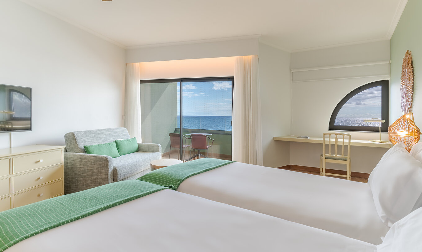 The Classic Sea View room at Pestana Vila Lido Madeira features two beds, a desk, a sofa, and a balcony