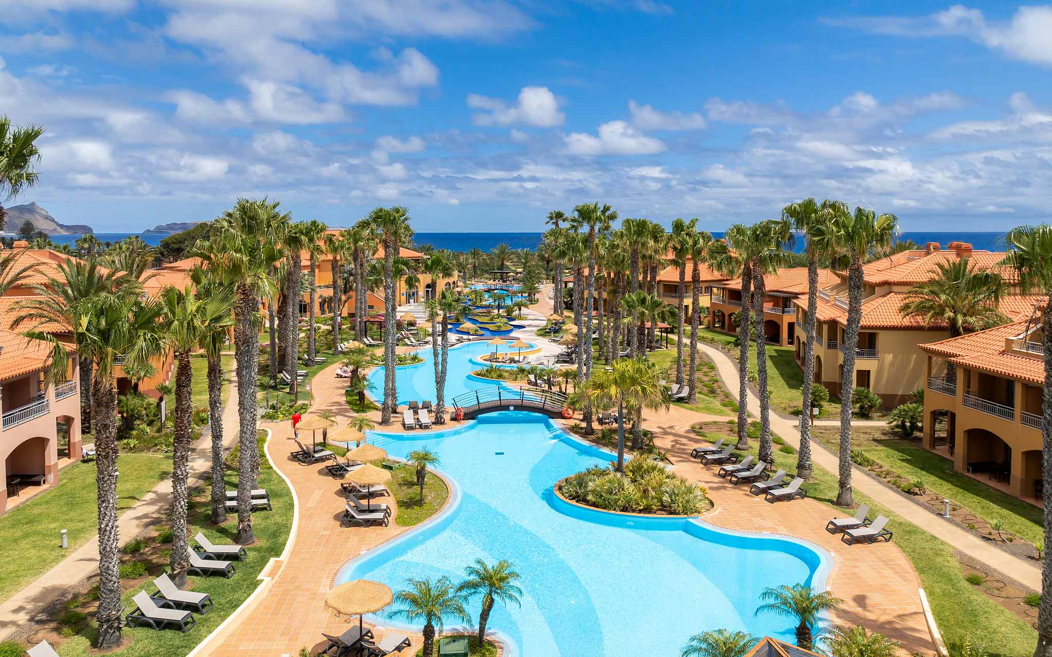 Swimming pool of the 5-star resort in Porto Santo, surrounded by tropical palm trees, sun loungers, and a garden.