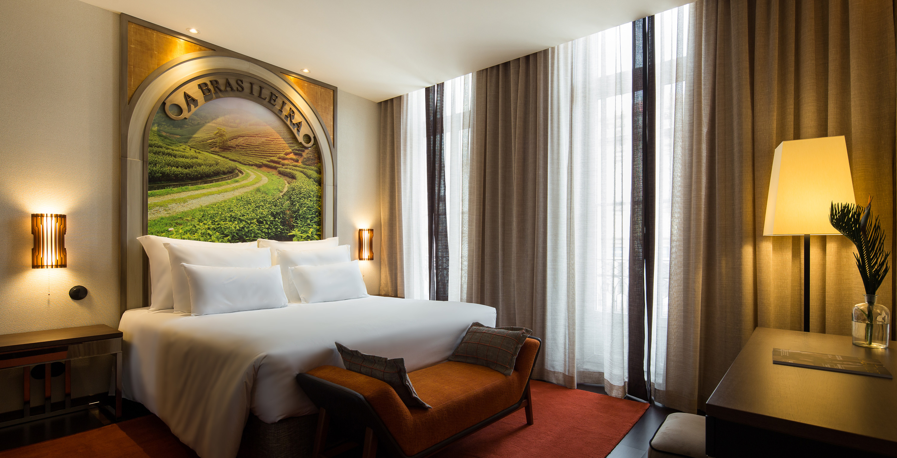 The Deluxe Superior do Pestana Porto - A Brasileira has a bed with a themed mural on the headboard and a bench at the back