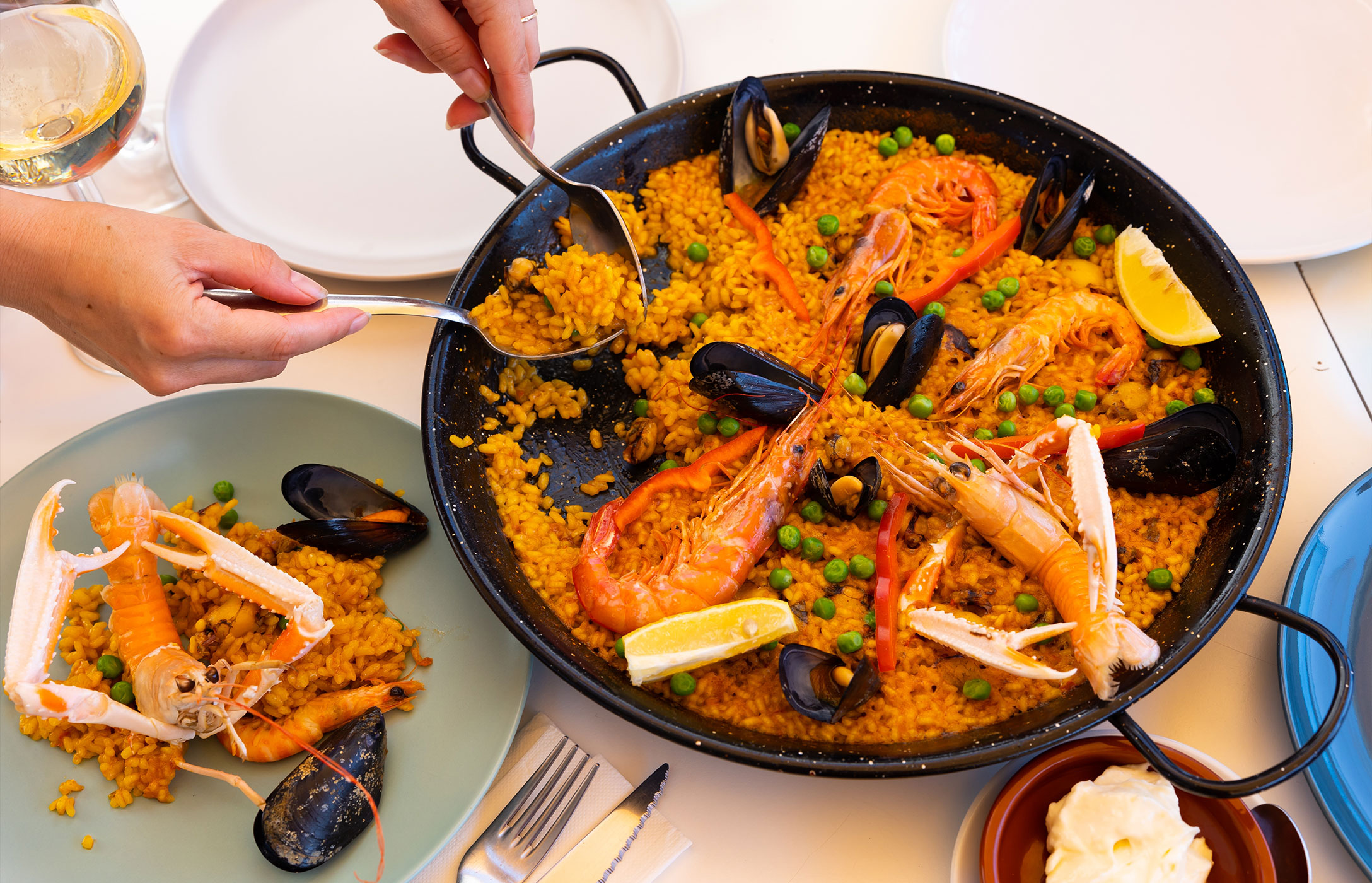 Person serving the typical Spanish dish, a paella pan, prepared with mussels, shrimp, peas, and rice