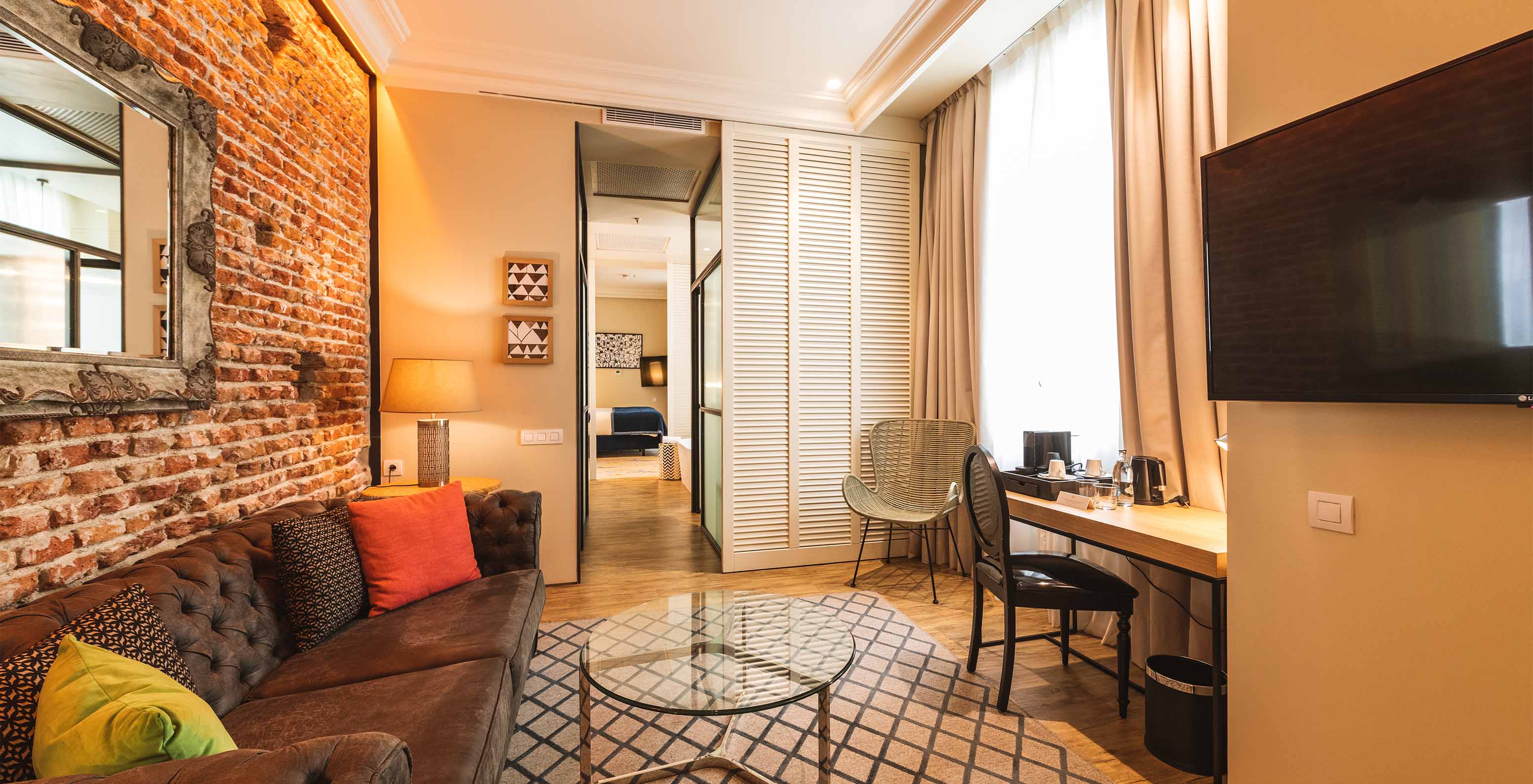 The Suite at Pestana Collection Plaza Mayor has a living room with desk, sofa, TV and a brick wall