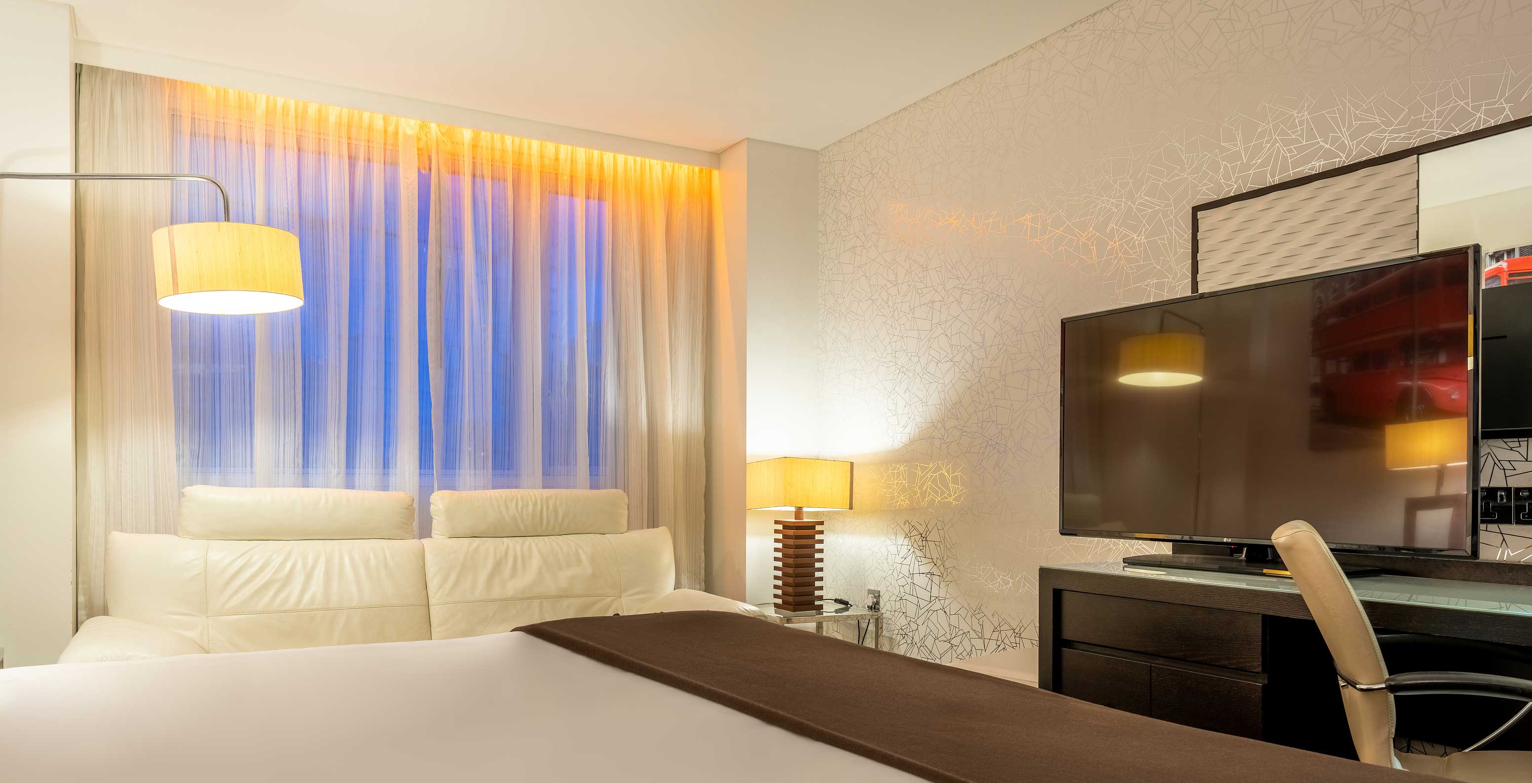 The Standard Disability at Pestana Chelsea Bridge has bed, desk with TV and chair, sofa and windows facing the city