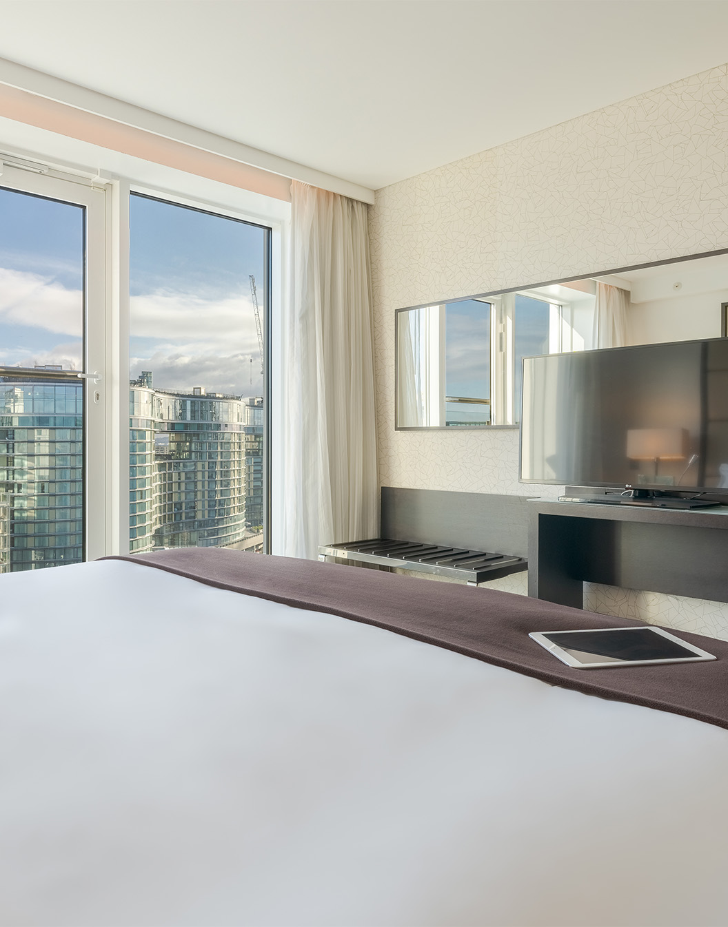 Room with a double bed, television, mirror, and large windows overlooking the city of London