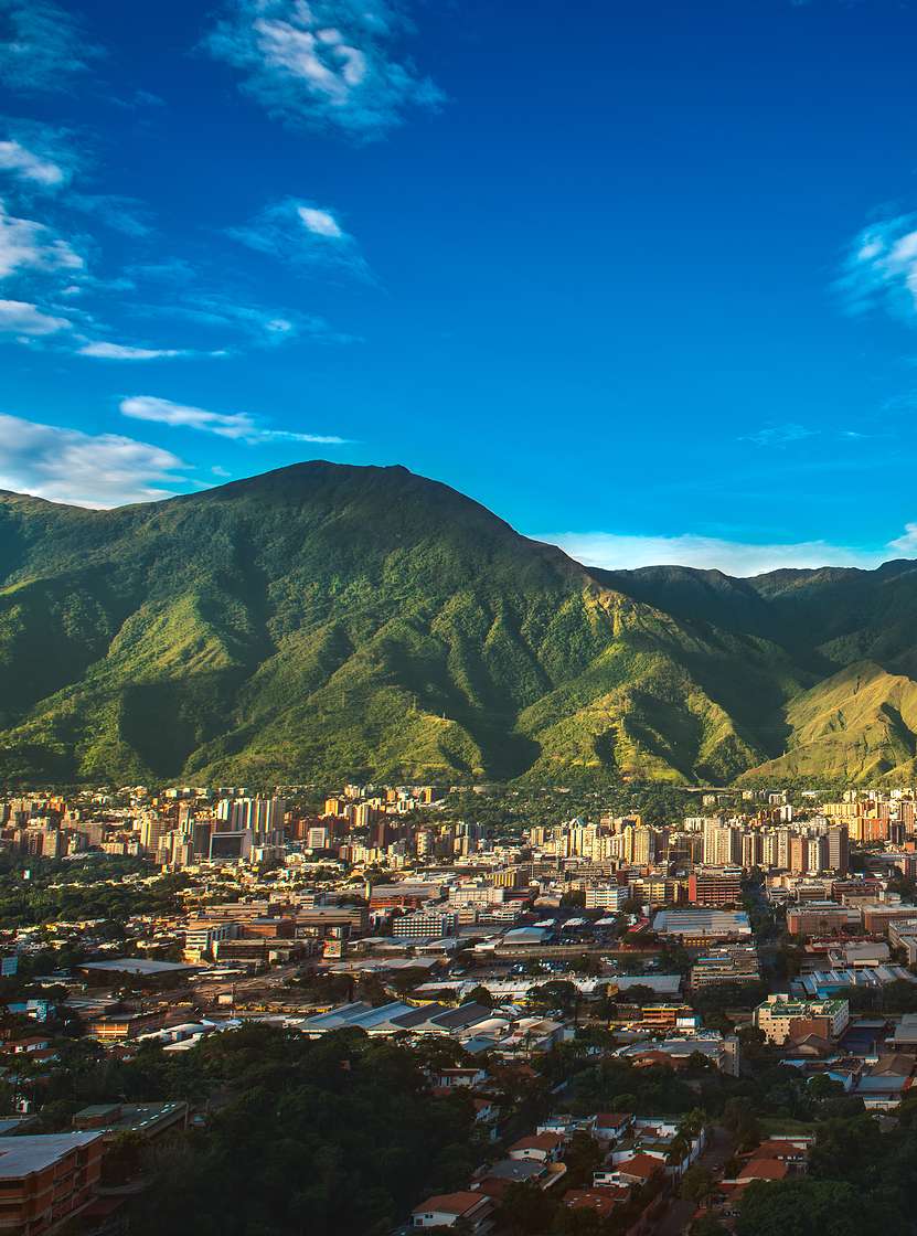 Aerial view of the city of Caracas, with tall buildings, contrasting with the mountainous nature, and the blue sky