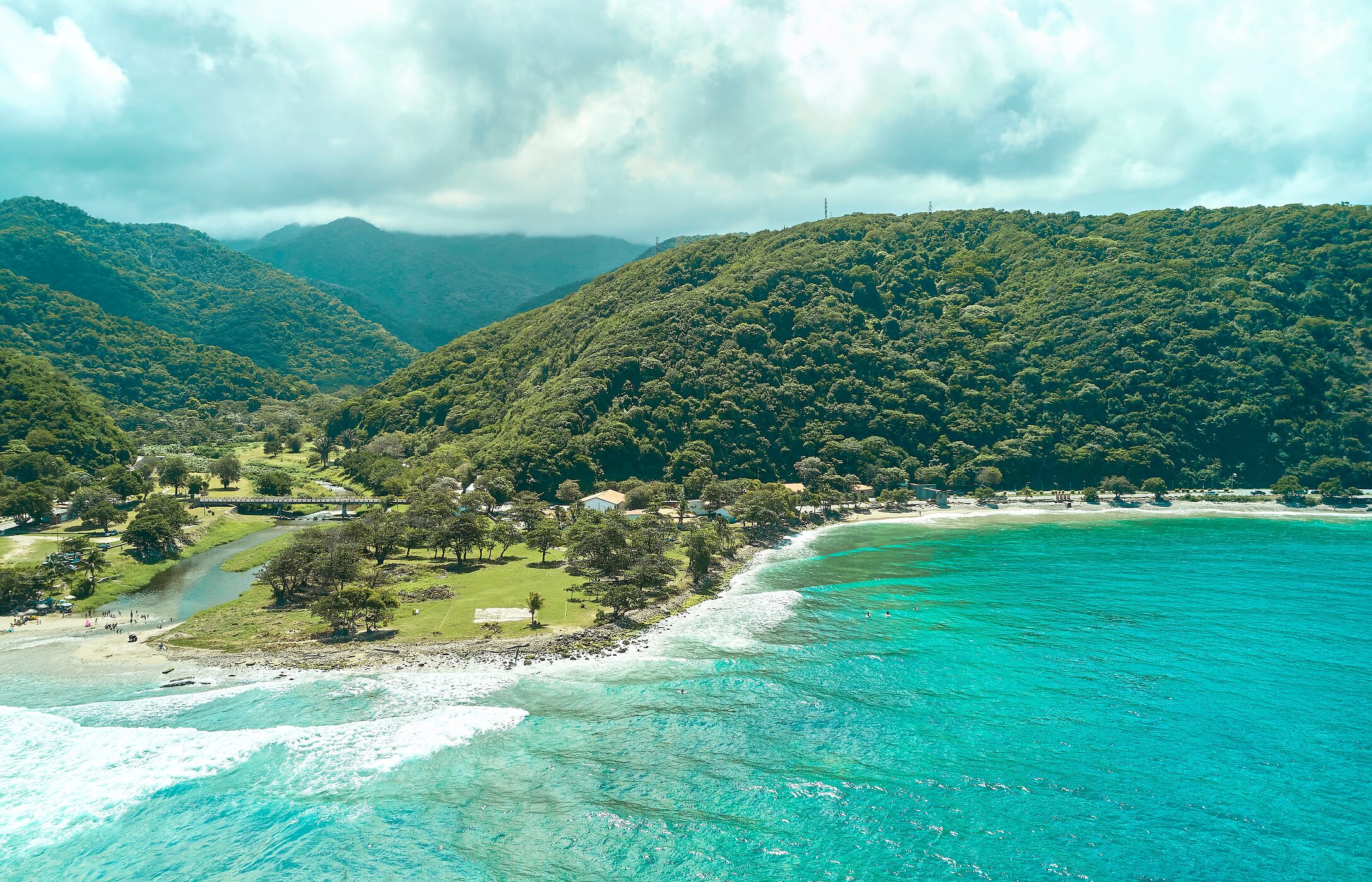 Aerial view of La Punta Beach in Venezuela, with crystal-clear waters, surrounded by green mountains.